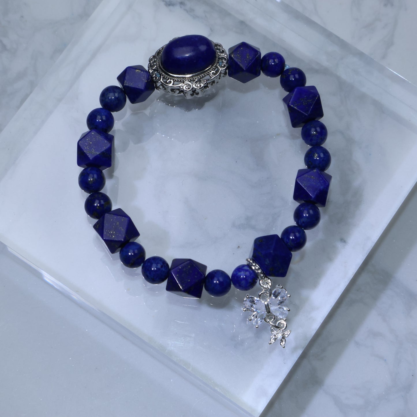 Flat lay of Lapis Lazuli bracelet with diamond-cut beads and ornate centerpiece on marble platform