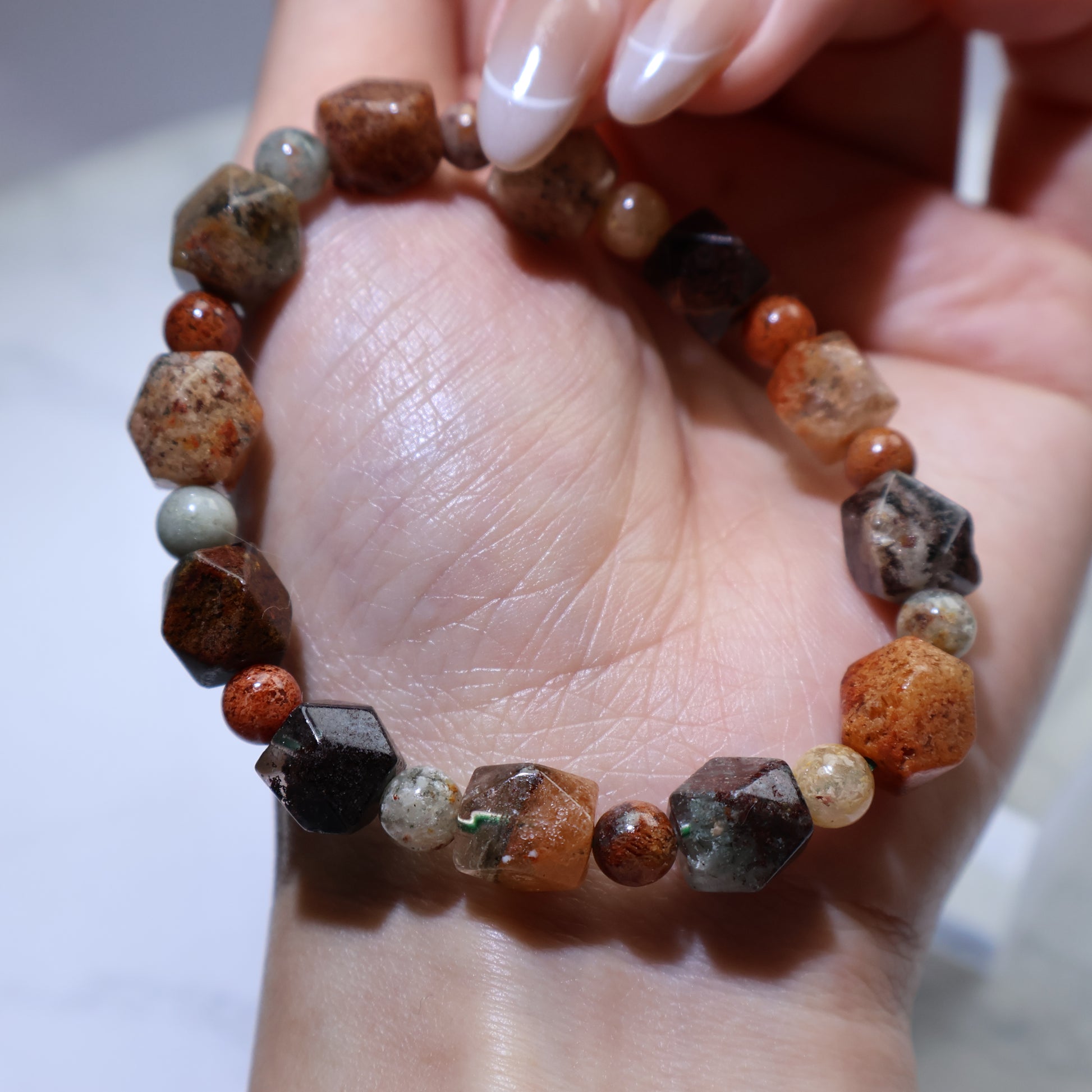 Handheld view showing geometric faceted beads in earthy reds, browns and greens