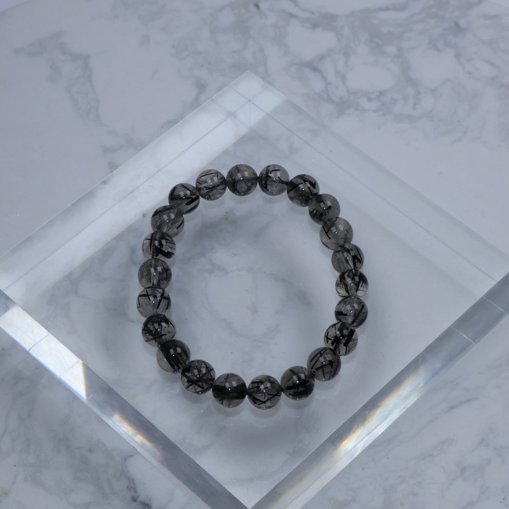 Top-down view of Black Rutilated Quartz bracelet on clear acrylic block