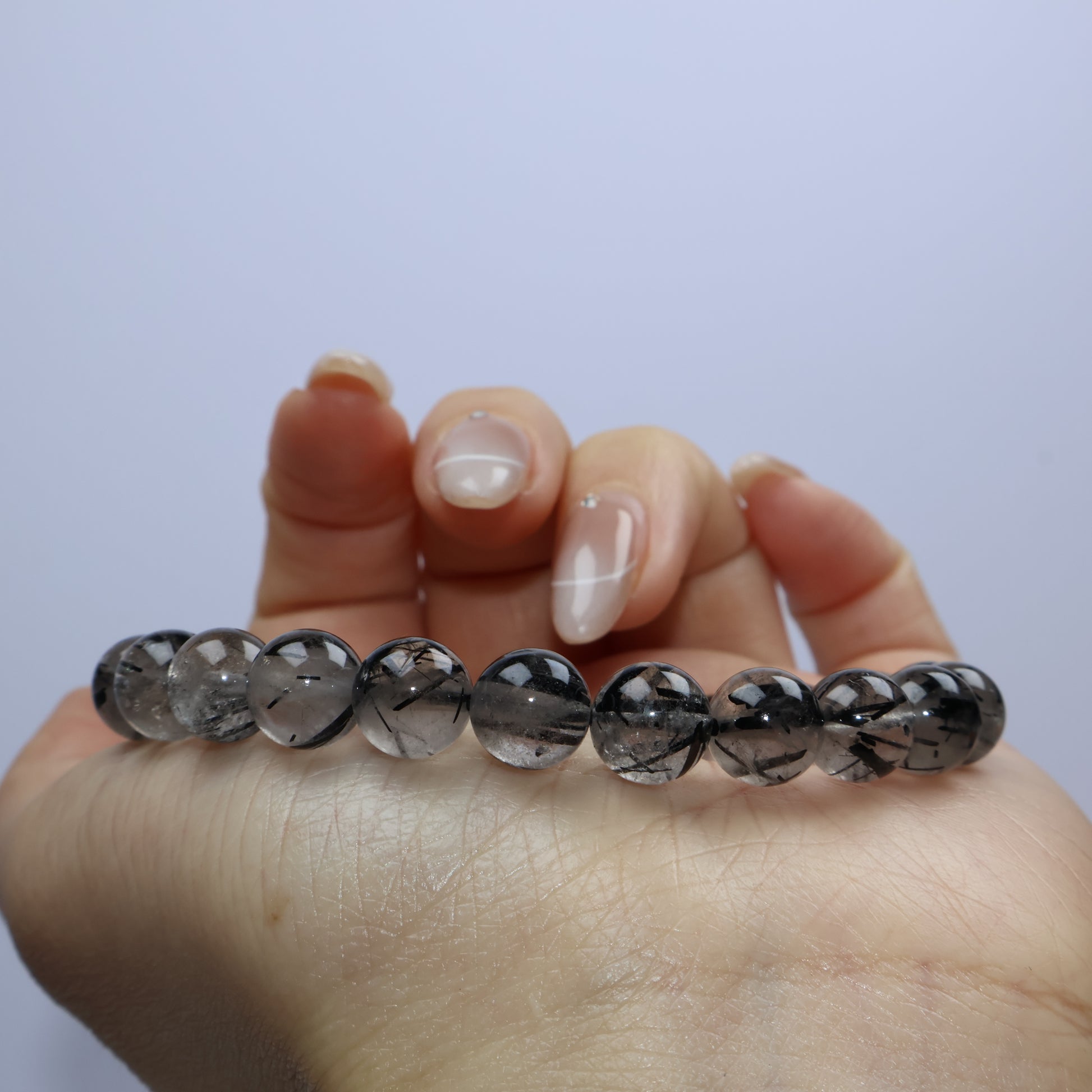 Close-up of rutile-rich quartz beads held between fingers