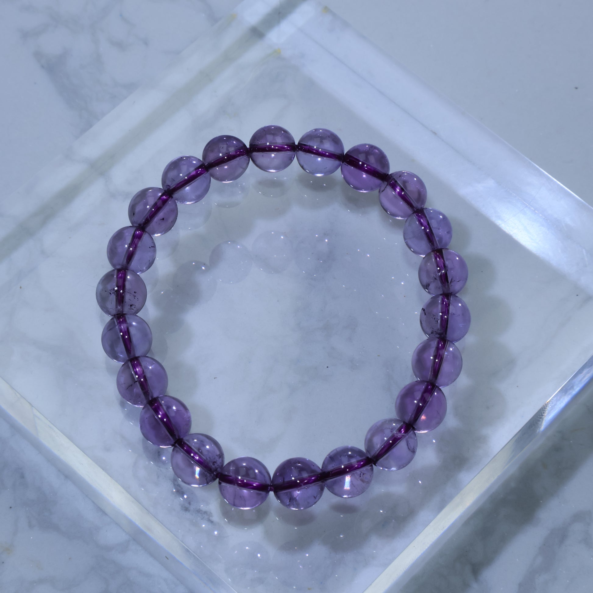 Overhead view of 9mm Dreamlight Amethyst bracelet on clear acrylic block, showing soft violet glow