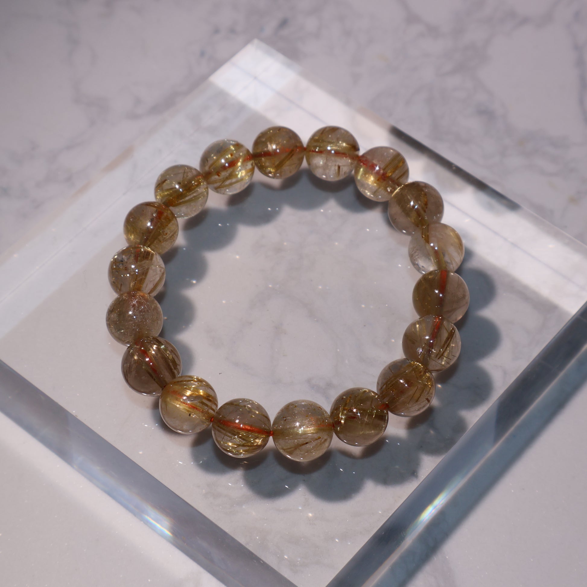 Flat lay of golden rutilated quartz bracelet on clear acrylic block, 11mm beads