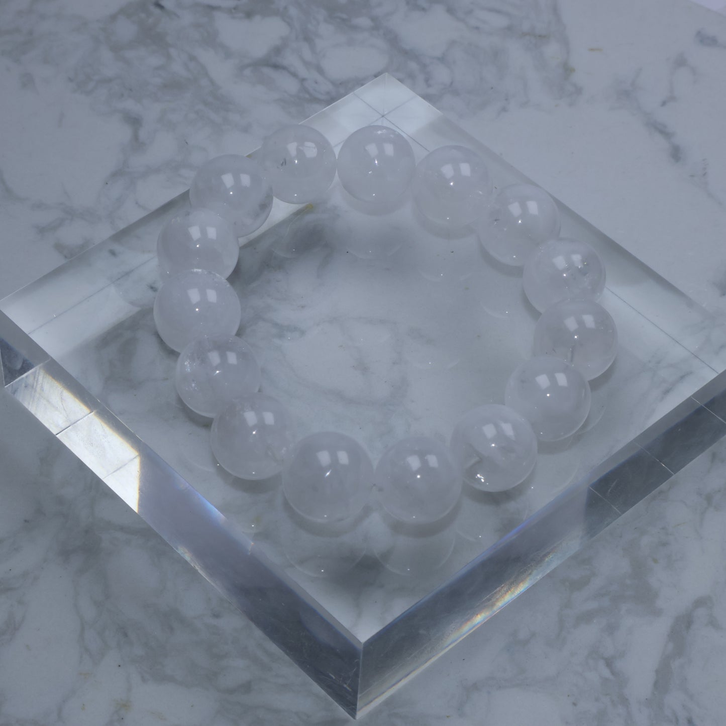 Top-down view of 15mm White Phantom Quartz bracelet on acrylic block, showing full circle of cloudy beads