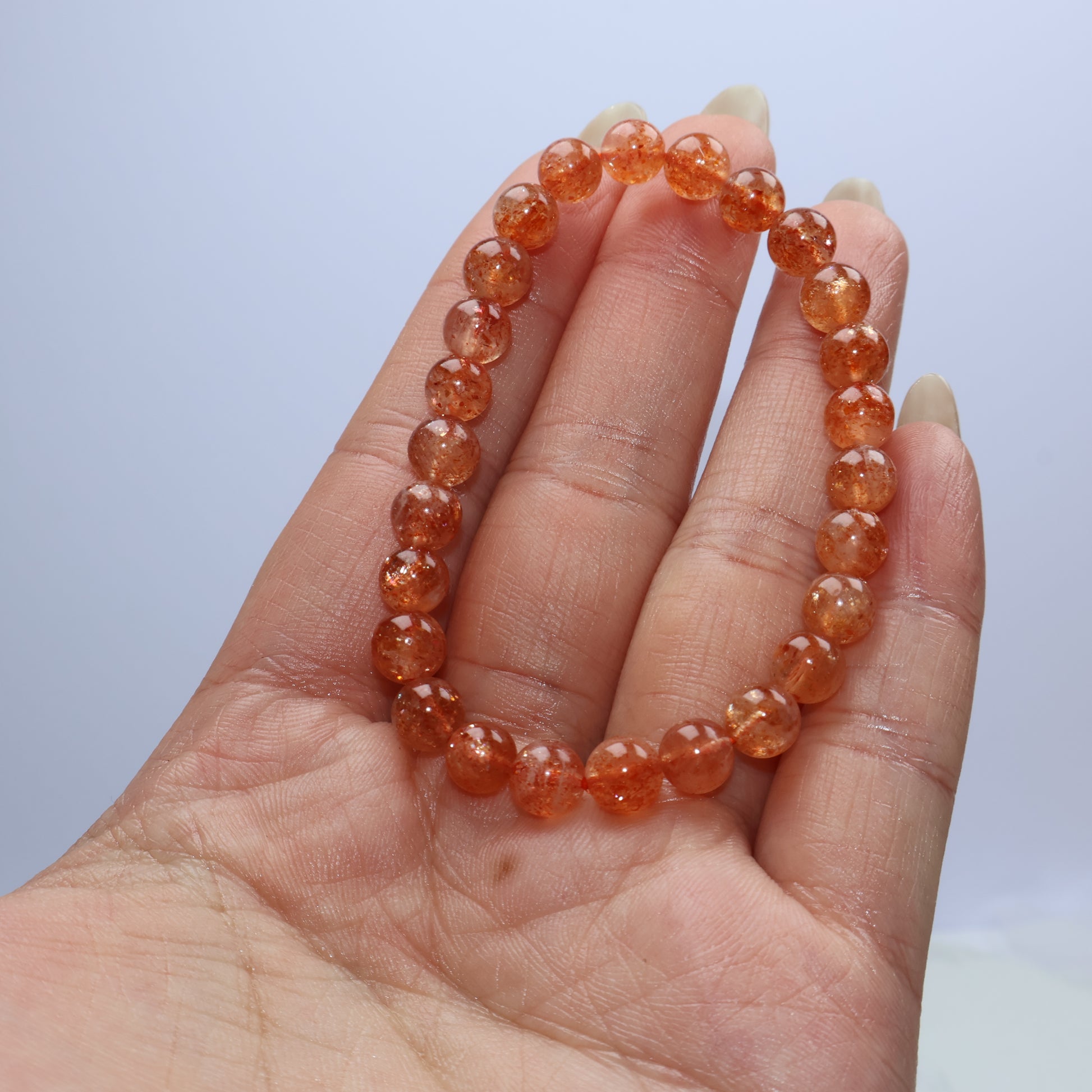 Handheld photo of 6mm Sunstone bracelet showing warm orange sparkles