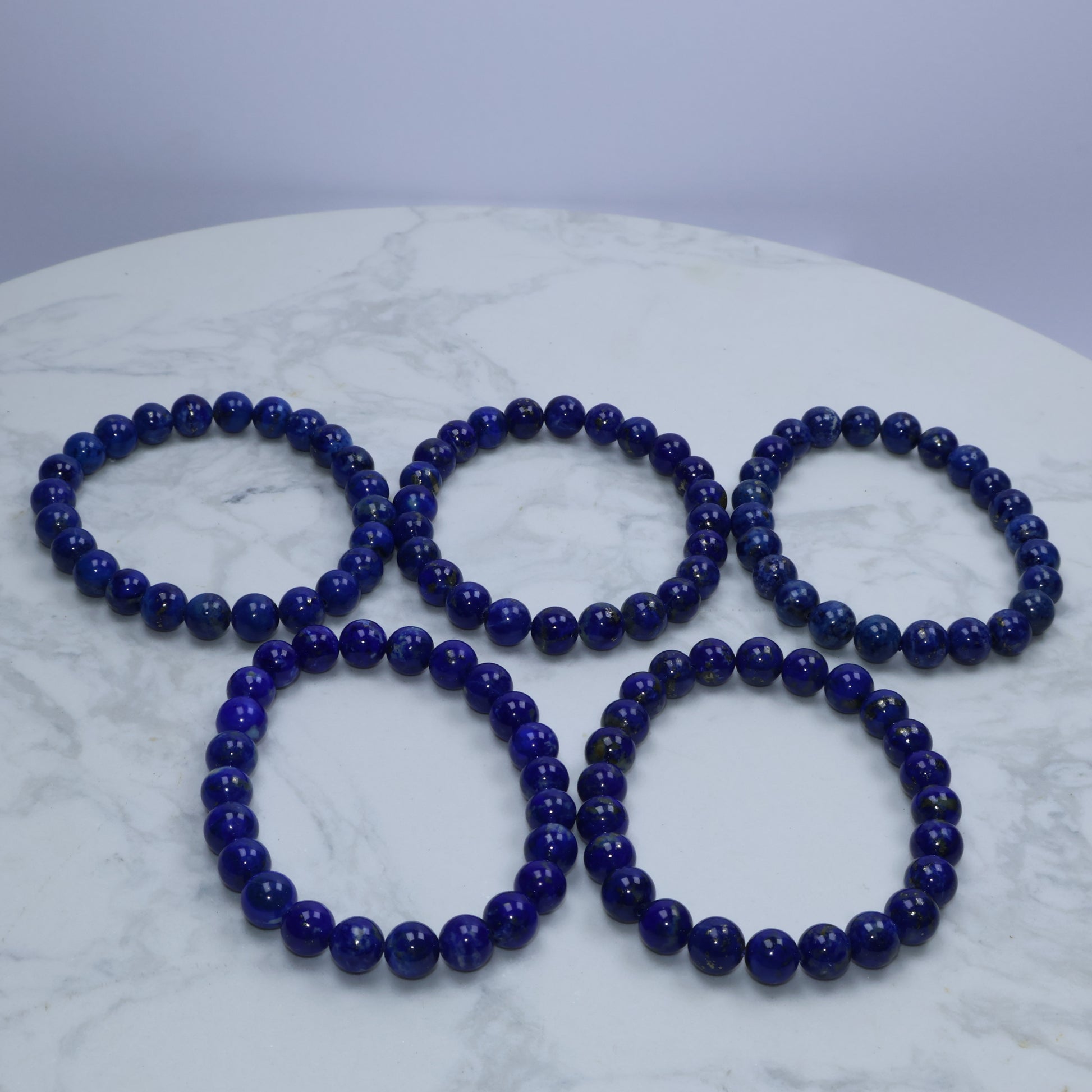 Flat lay of five 7mm lapis lazuli bracelets arranged on white marble surface – Starter Collection