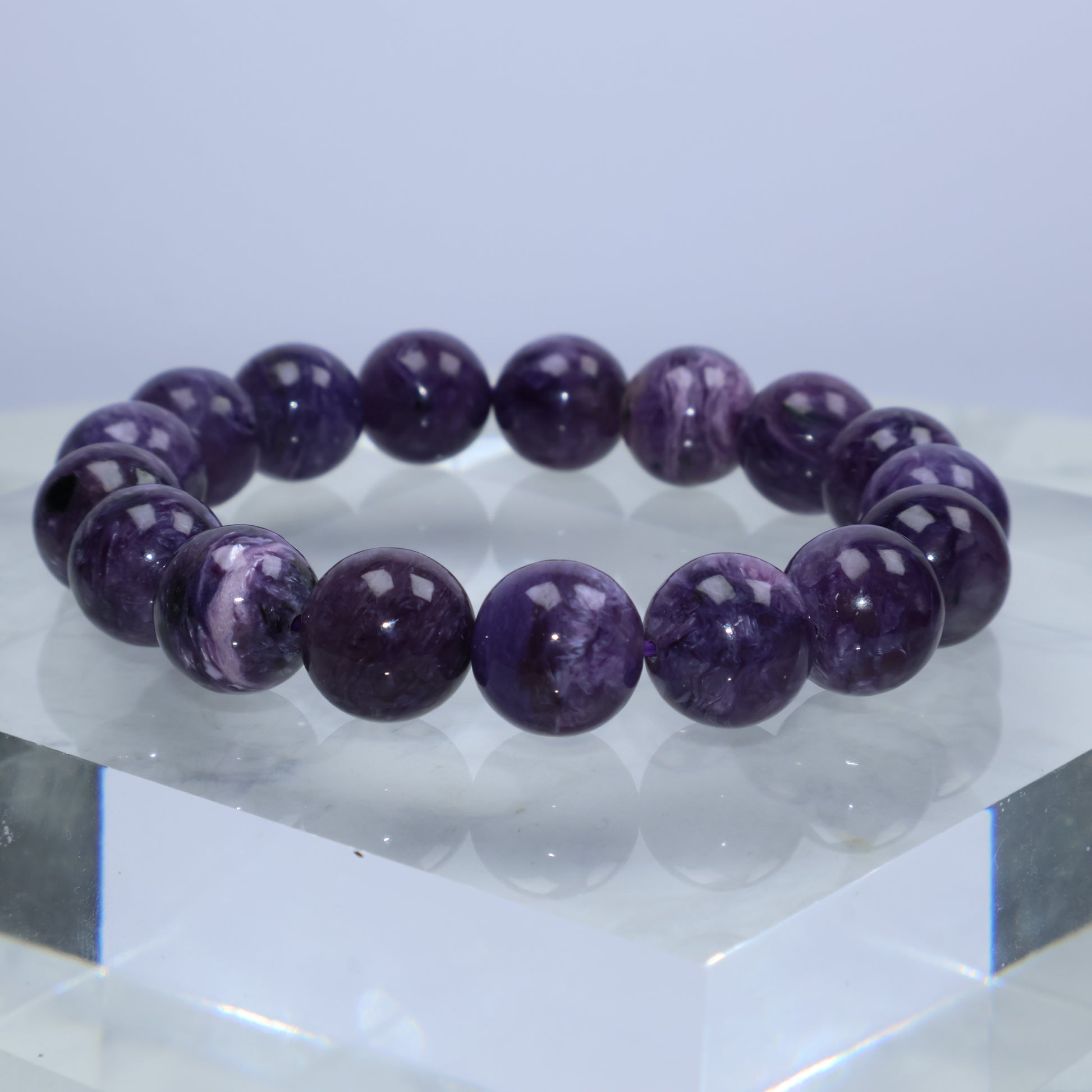 Purple Charoite bracelet displayed on clear block with glossy reflections