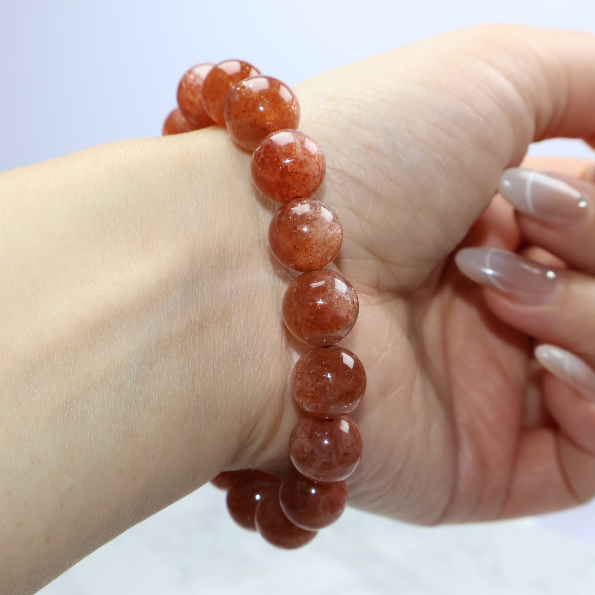 Wrist shot of 11mm Sunstone bracelet showing warm orange-red hues and natural sparkles despite minor inclusions.