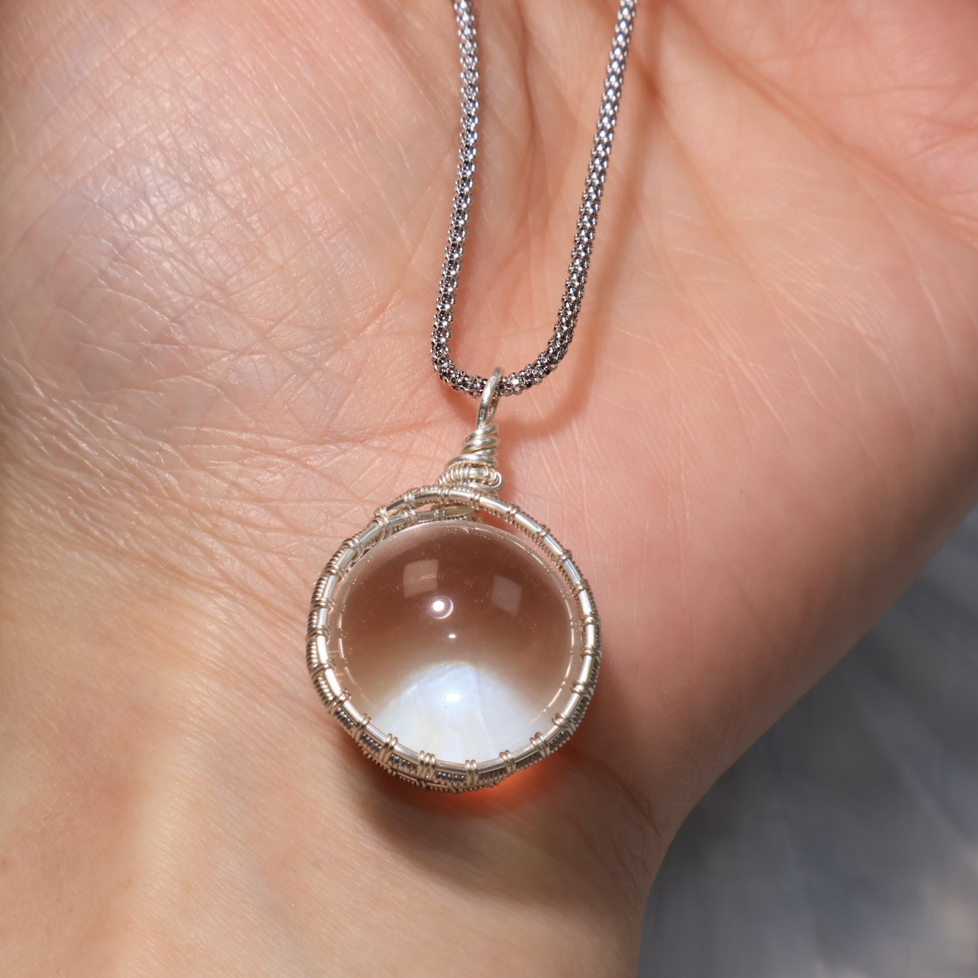 The pendant shown in hand, demonstrating size and light reflection of the 17.6mm Clear Quartz sphere.