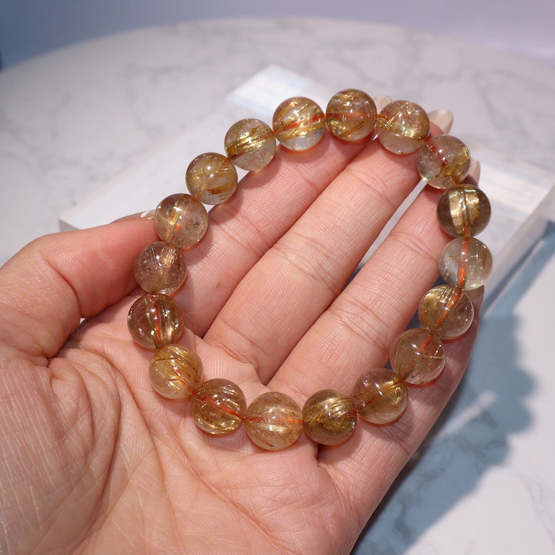 Handheld view of golden rutilated quartz bracelet showing rutile shine