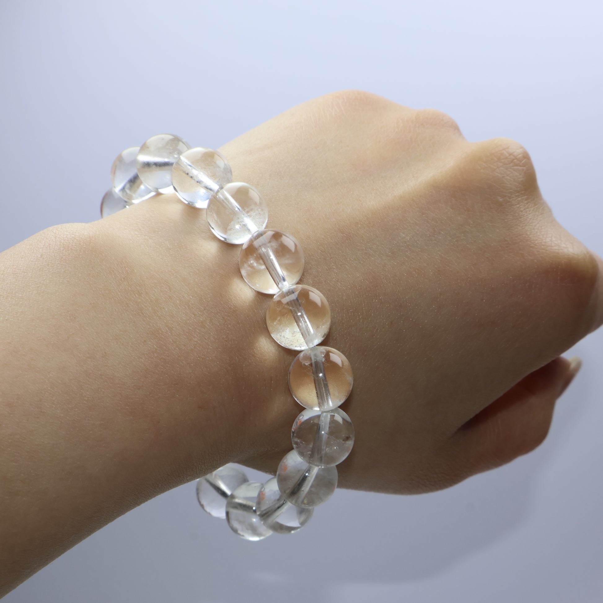 Clear quartz bracelet with 11mm beads worn on wrist, showing natural clarity and slight inclusions under soft light