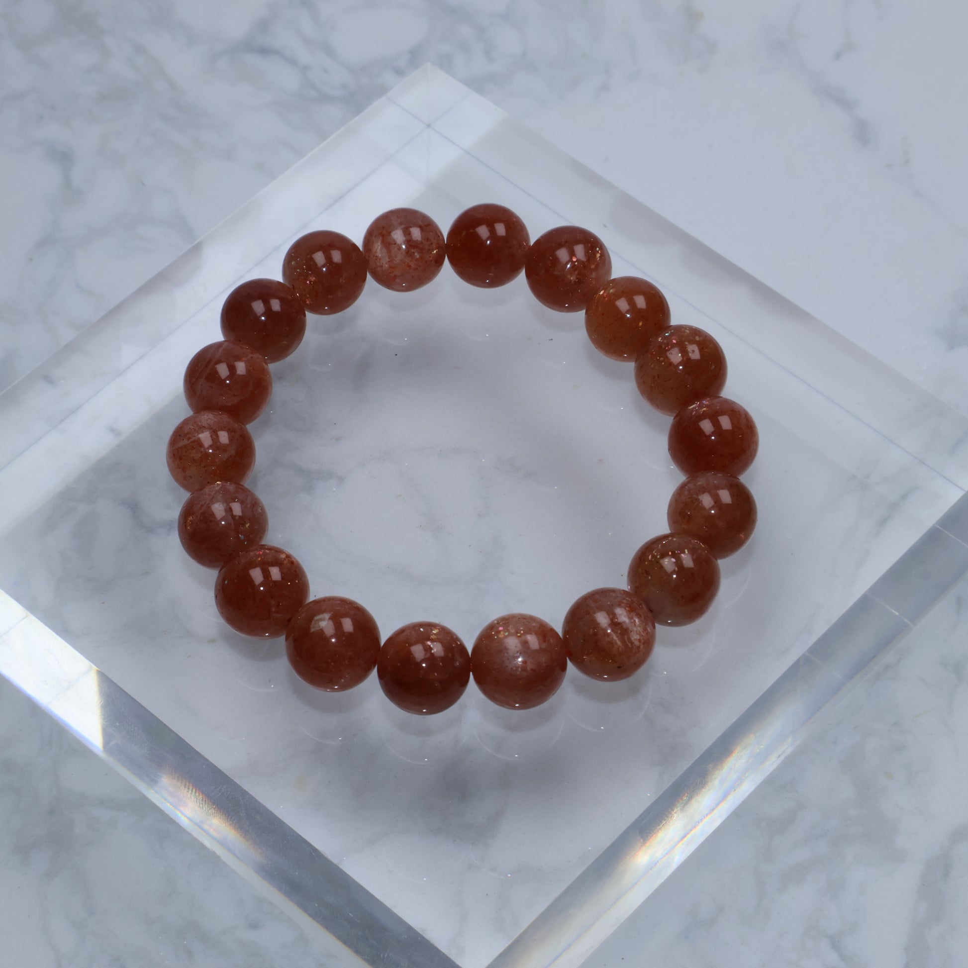 Close-up of 11mm Sunstone bracelet on clear acrylic, showing deep orange color and subtle sparkles
