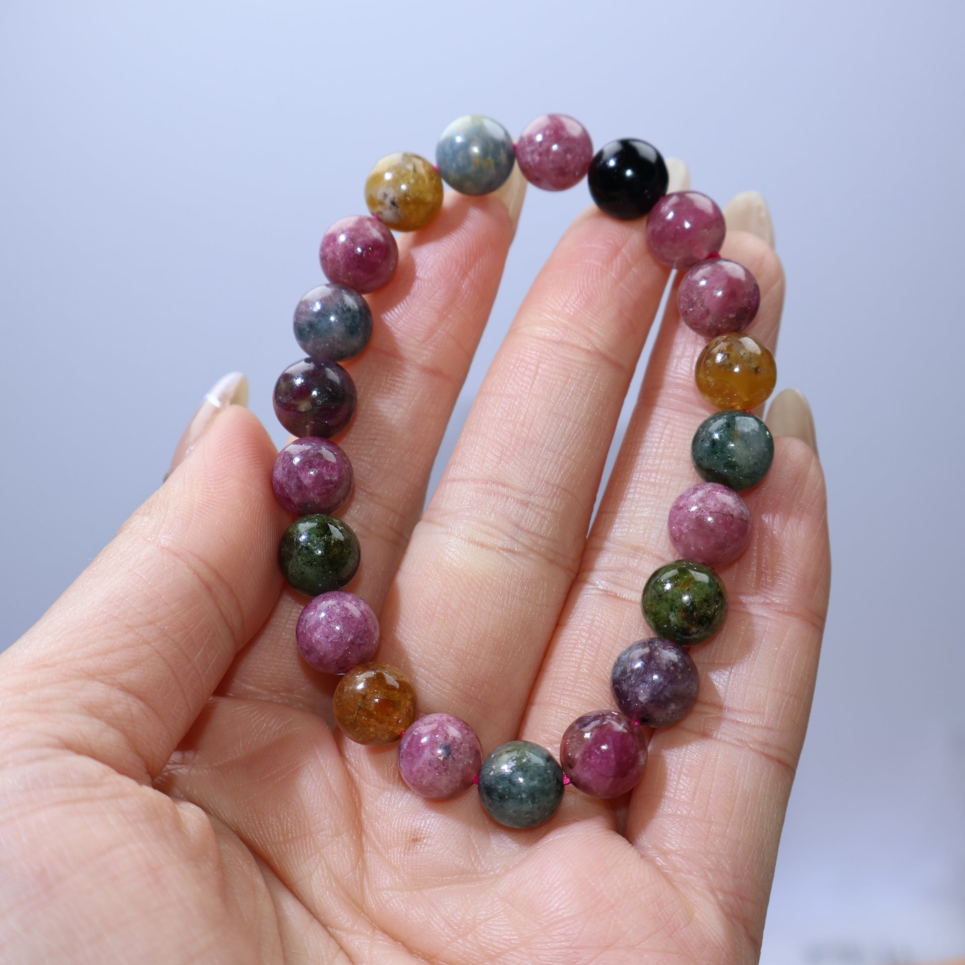 Handheld view of multicolor tourmaline bracelet showing pink, green, yellow, blue, and black beads