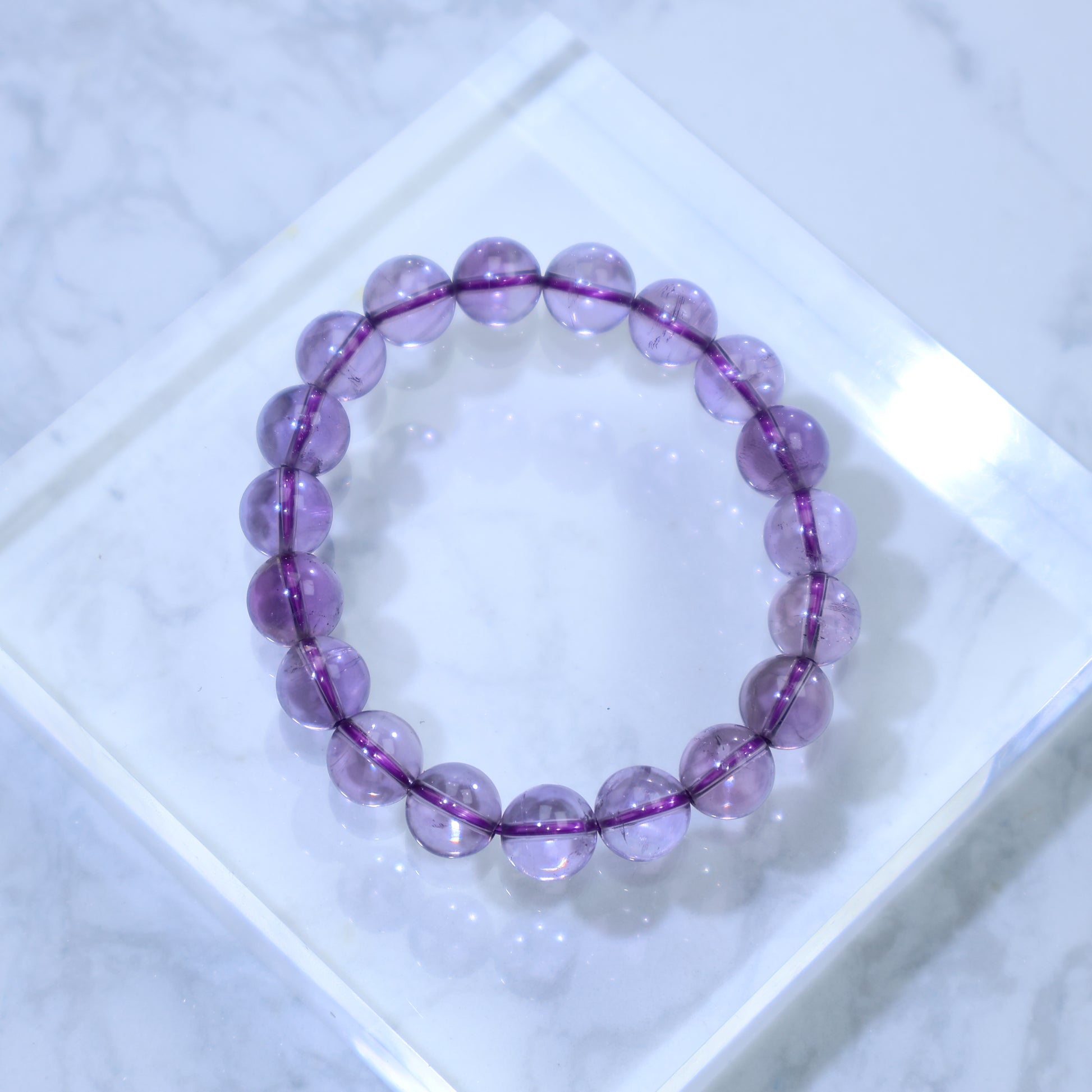 Top-down view of high-clarity amethyst bracelet on white marble background