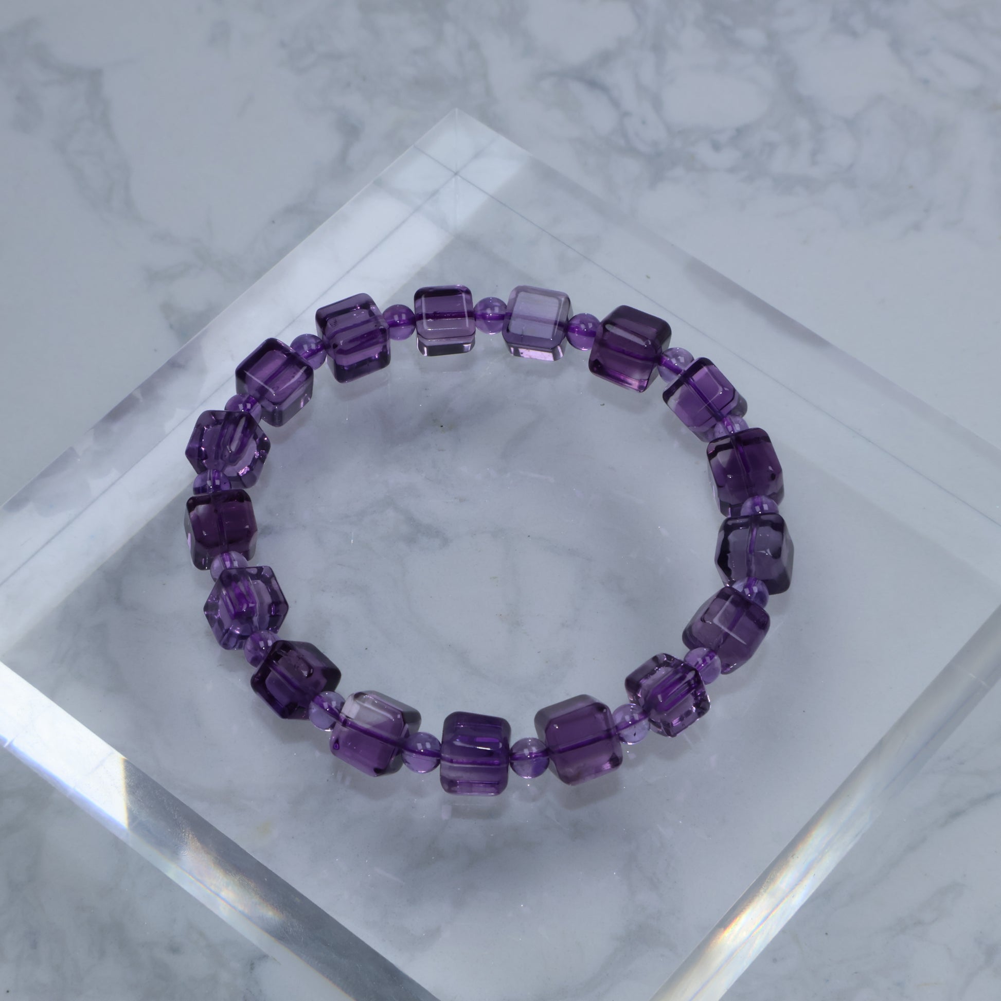 Top-down photo of square-cut Amethyst bracelet on acrylic block with marble background