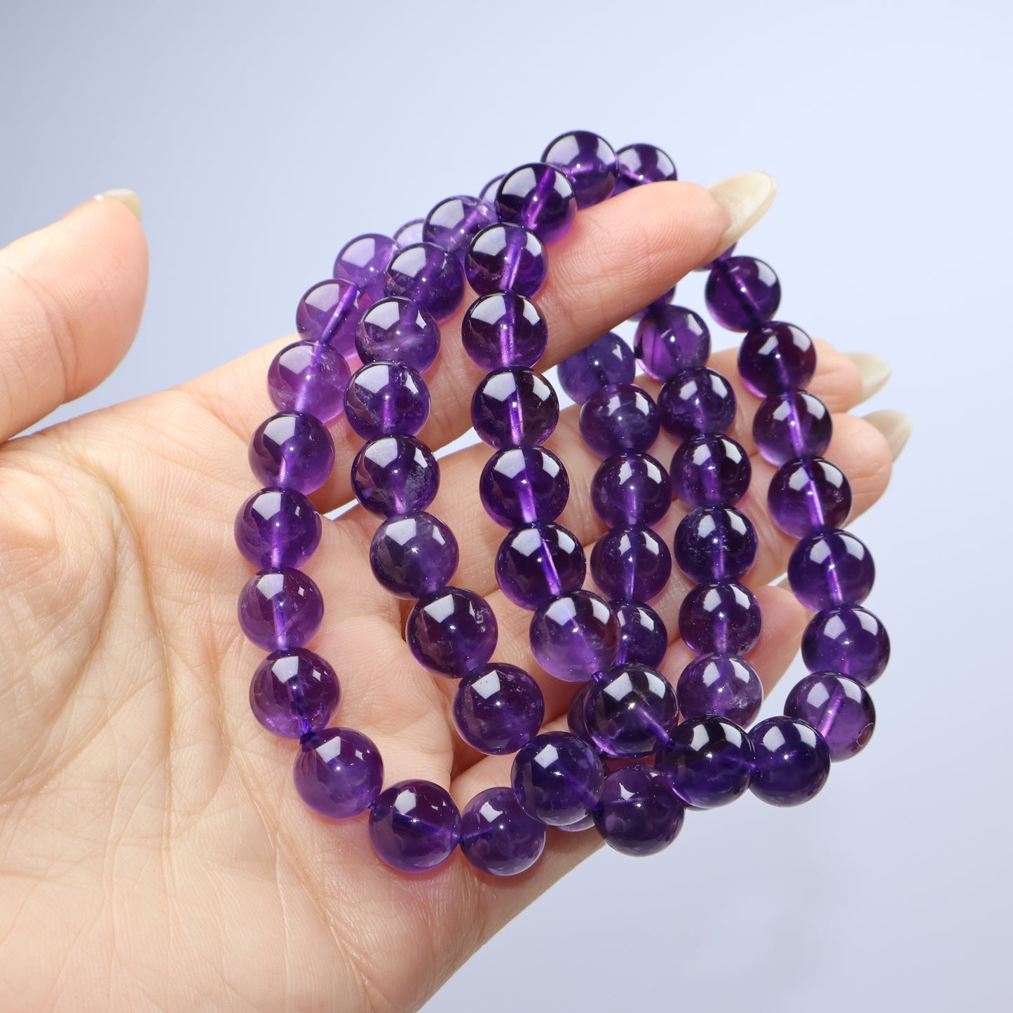 Handheld view of multiple strands of 9mm Amethyst beads showing deep purple color and high polish