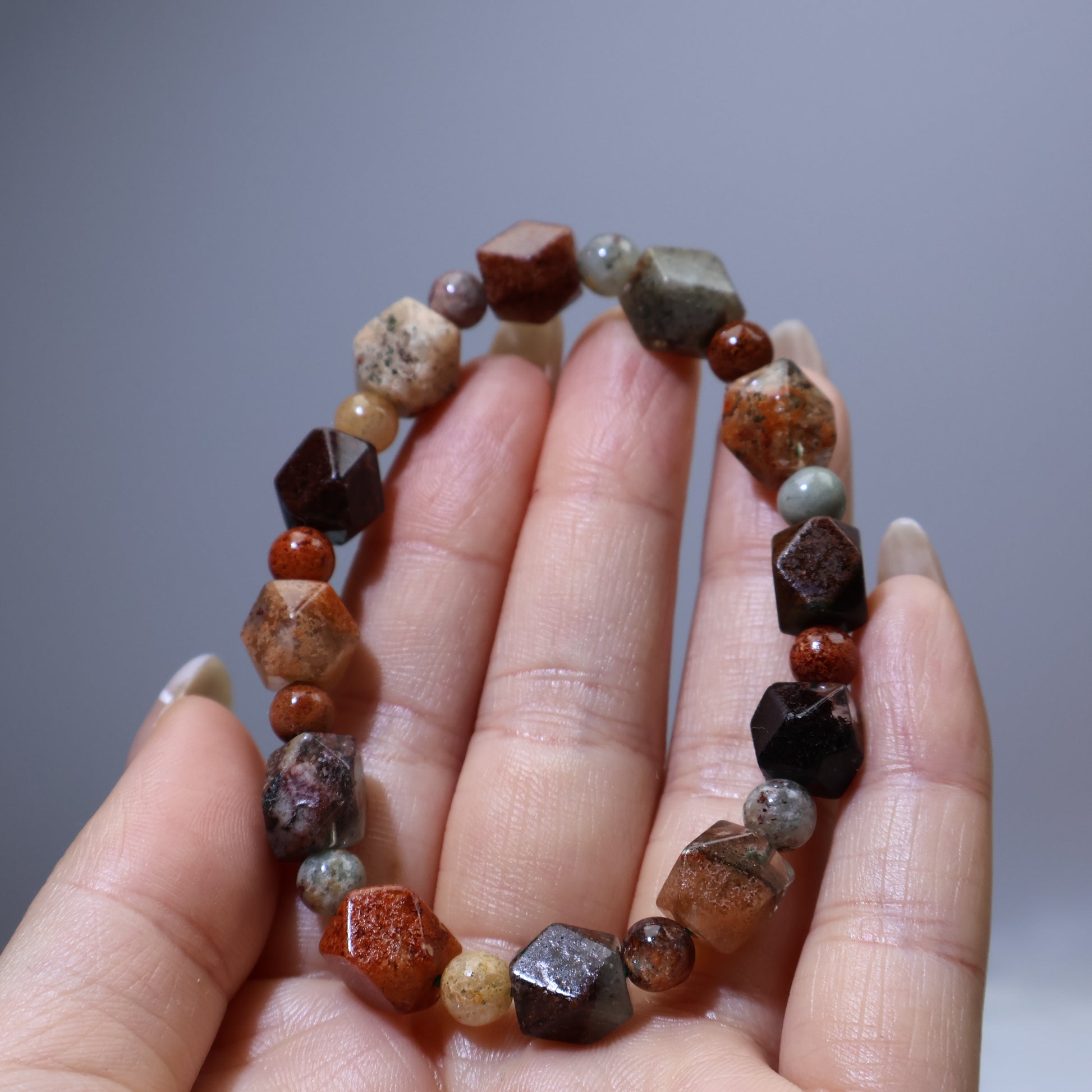Handheld view showing geometric faceted beads in earthy reds, browns and greens