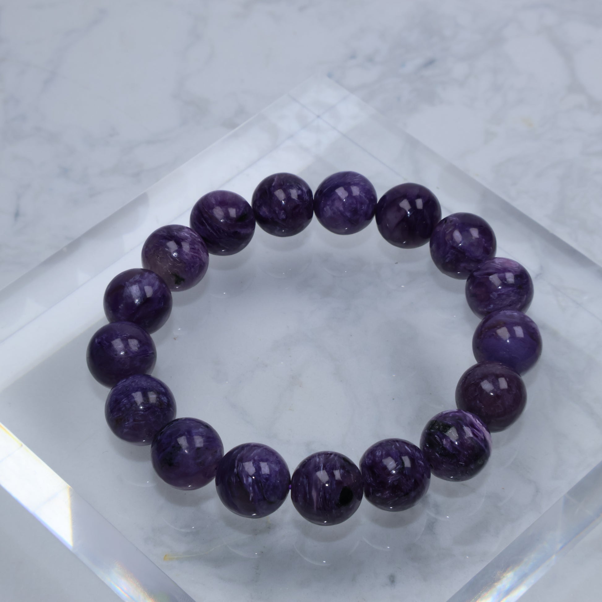 Top-down view of dark purple Charoite bracelet on acrylic cube with marble background