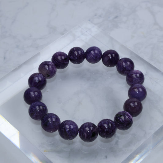 Top-down view of dark purple Charoite bracelet on acrylic cube with marble background