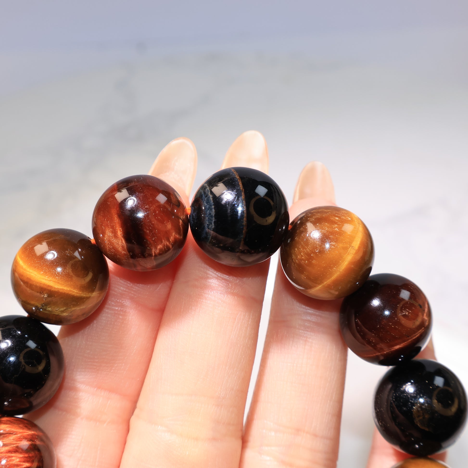 Close-up of bracelet between fingers, showing the deep blue tiger eye beads.