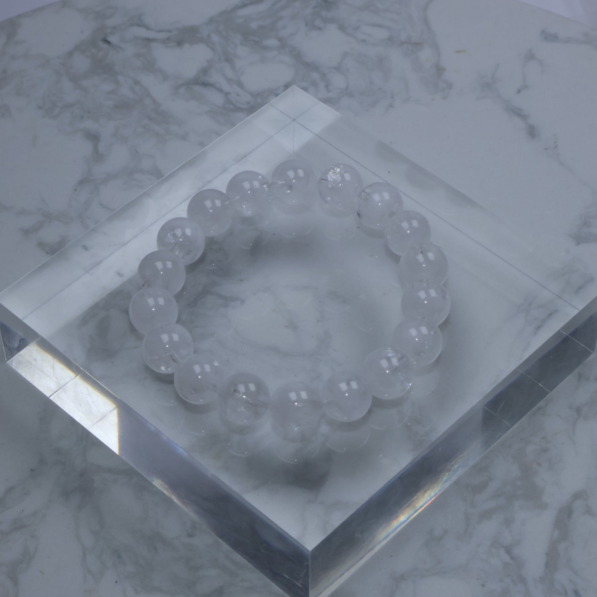 Top-down photo of White Phantom Quartz bracelet resting on clear acrylic cube