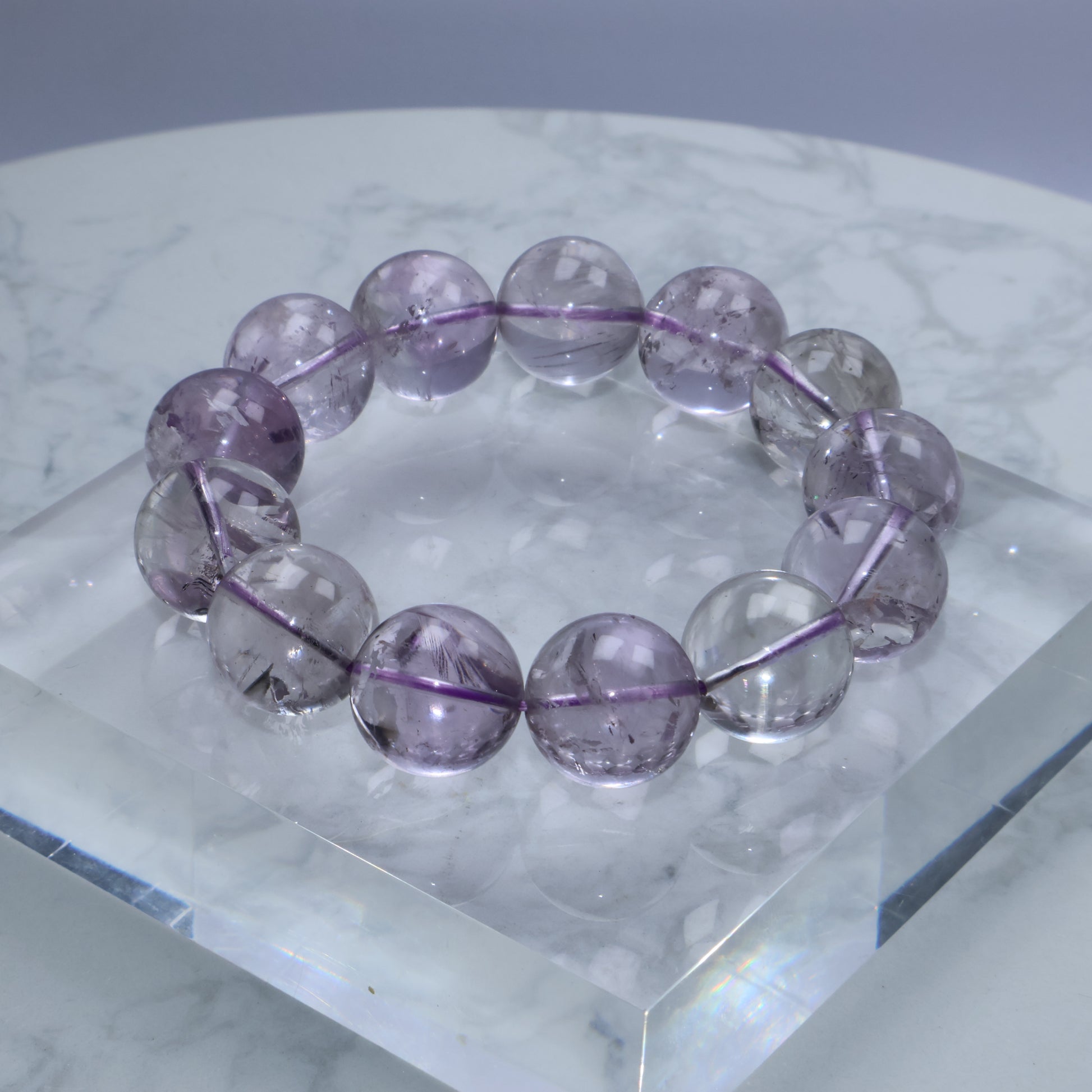 Close-up of translucent 17mm amethyst bracelet on a clear acrylic display