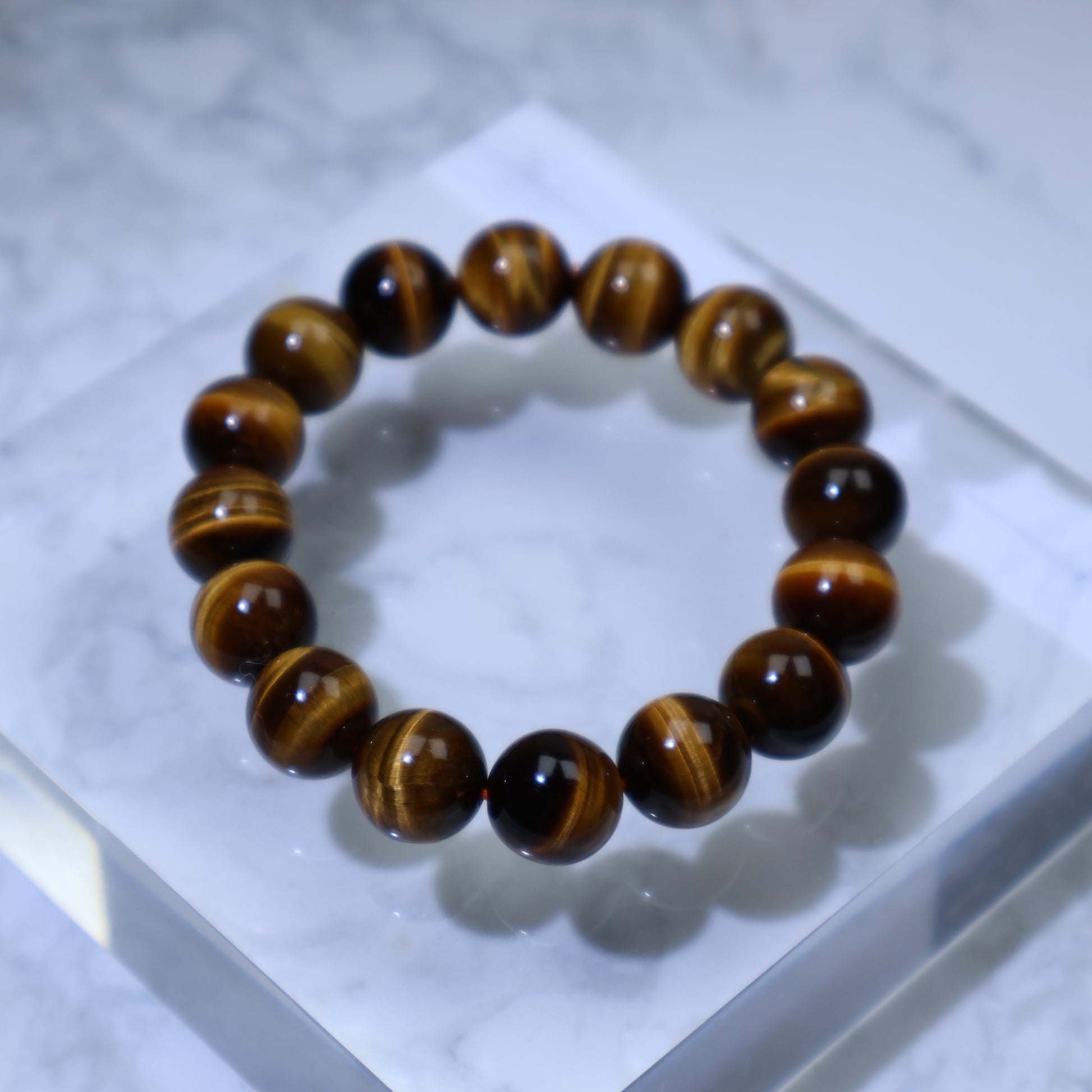Top-down view of Tiger’s Eye bracelet on clear acrylic block, showing golden-brown chatoyance