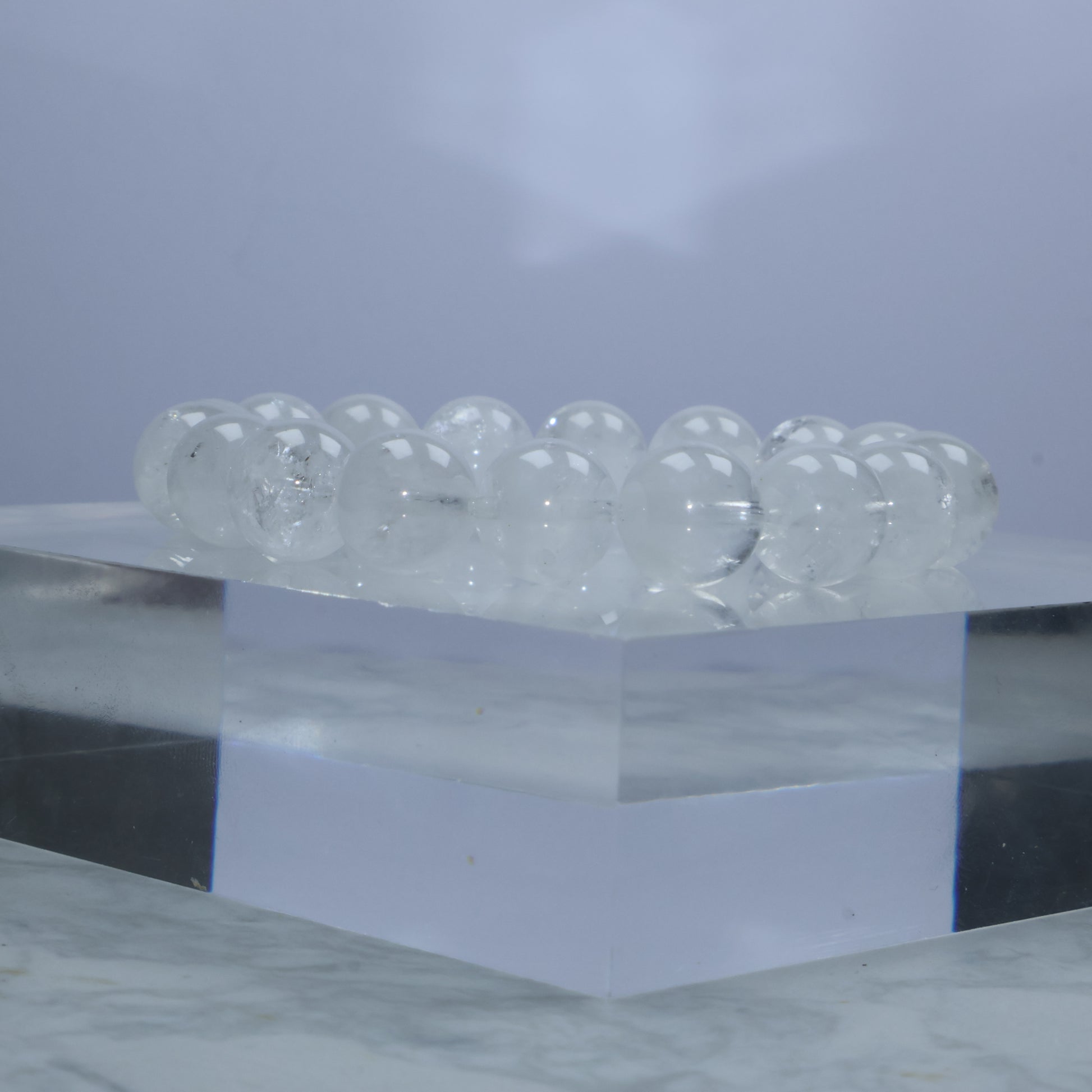 Side angle of a White Phantom Quartz bracelet displayed on a clear acrylic cube, showcasing the inner mist-like inclusions and high transparency.