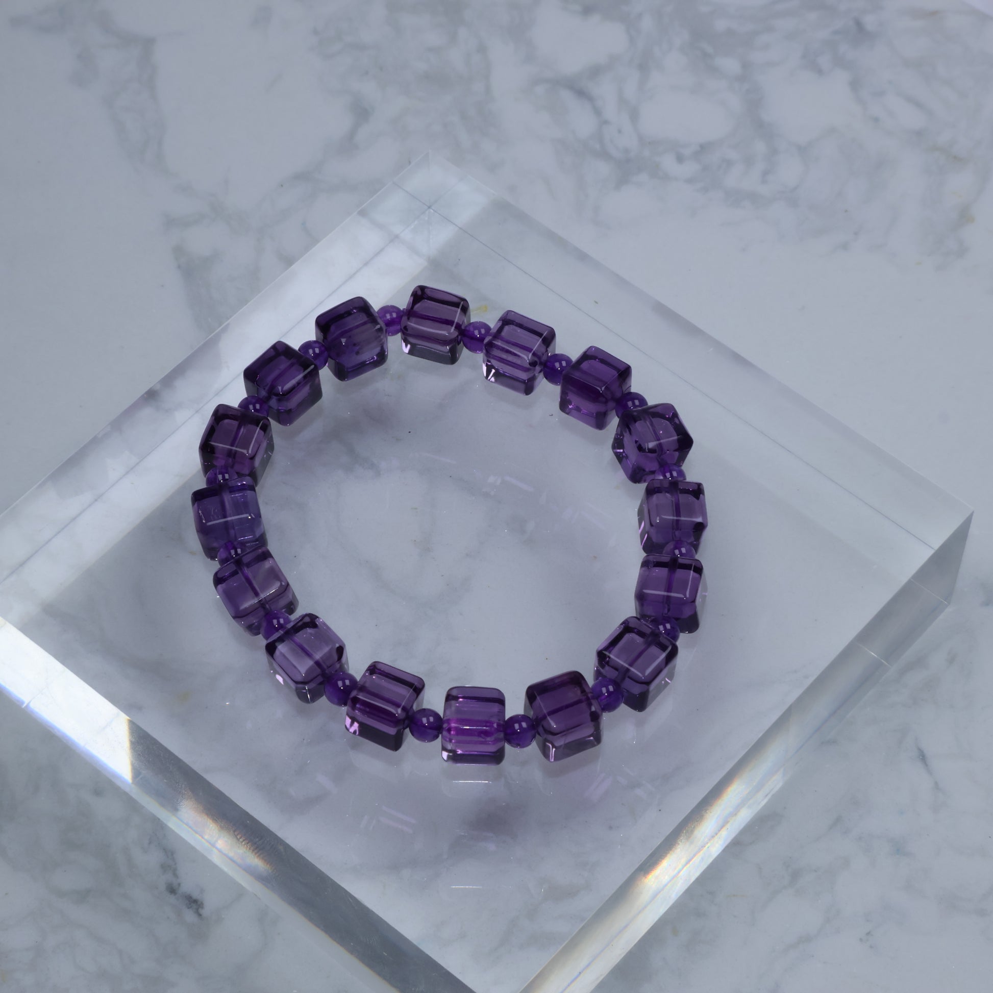 Top-down photo of amethyst square bead bracelet on clear acrylic cube with marble background
