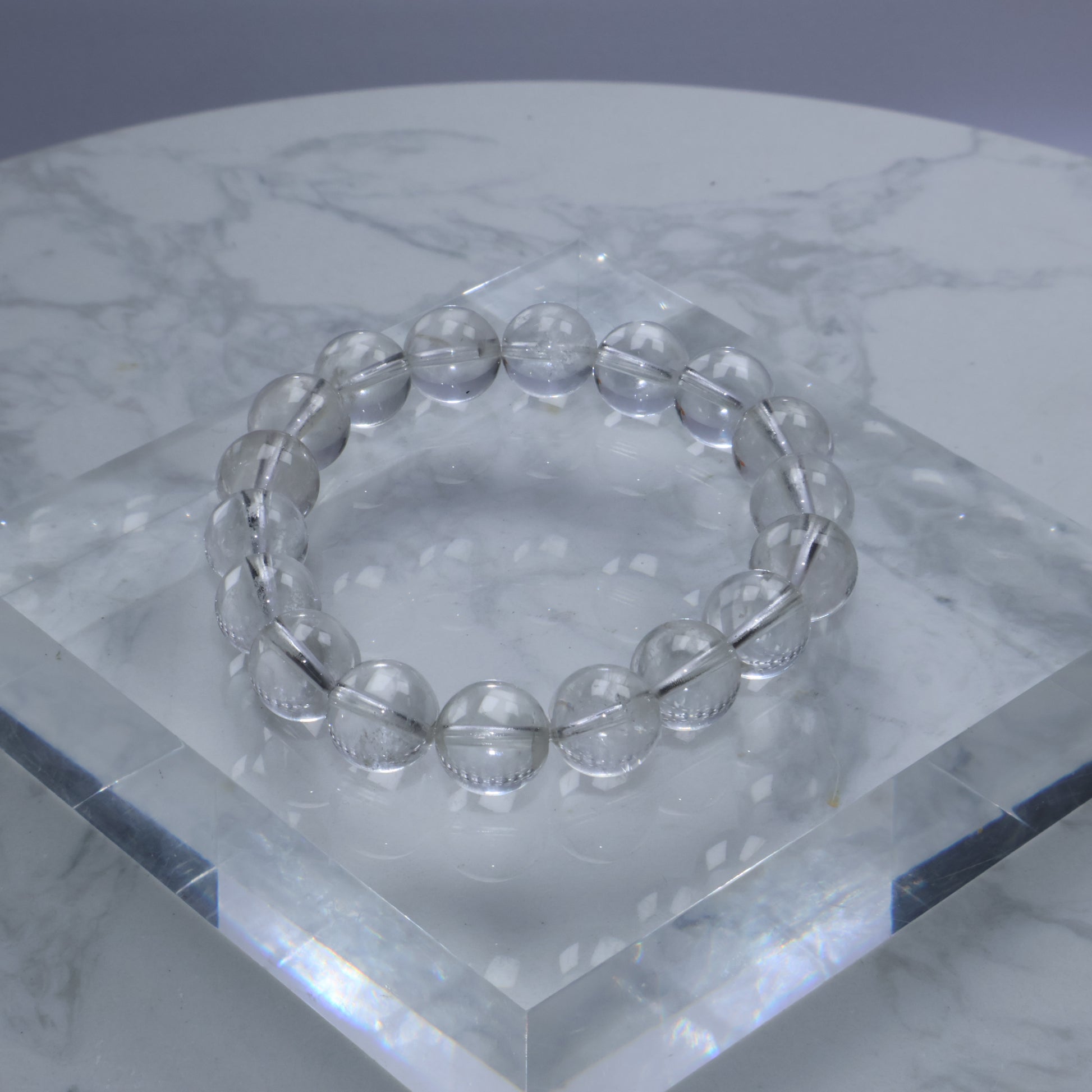 Clear quartz bracelet with 11mm round beads displayed on a crystal acrylic stand