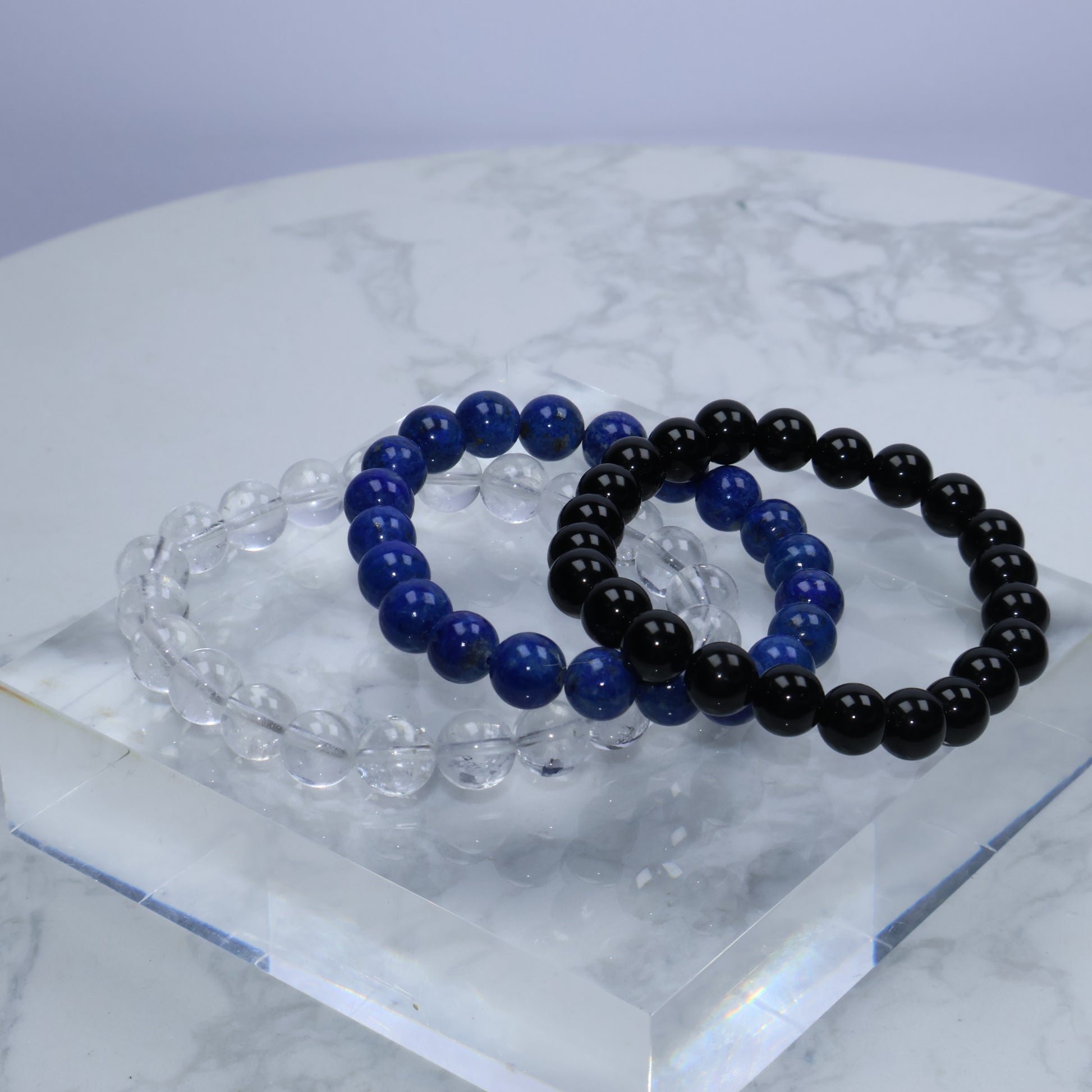 Flat lay of Clear Quartz, Lapis Lazuli, and Black Obsidian bracelets on round marble plate – Crystal Beginner Set