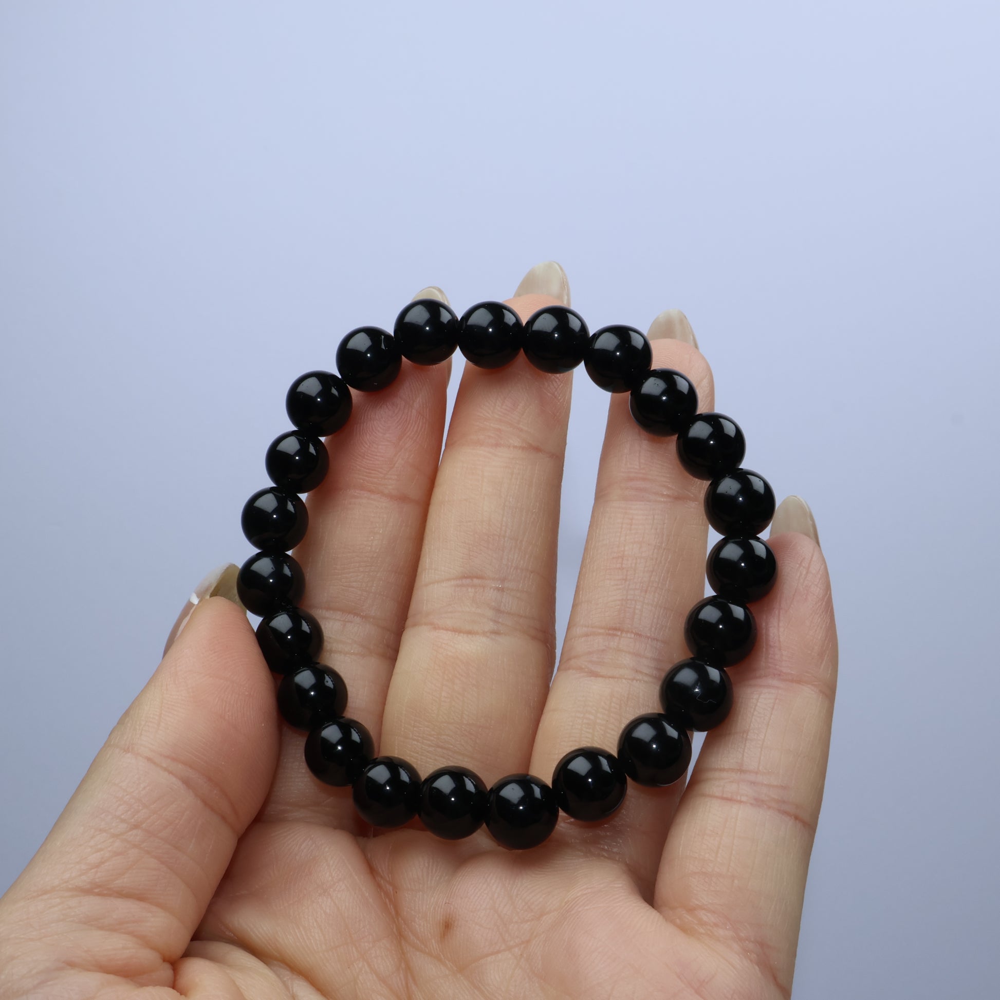 Flat lay of a black obsidian bracelet on a soft beige marble surface with diffused lighting