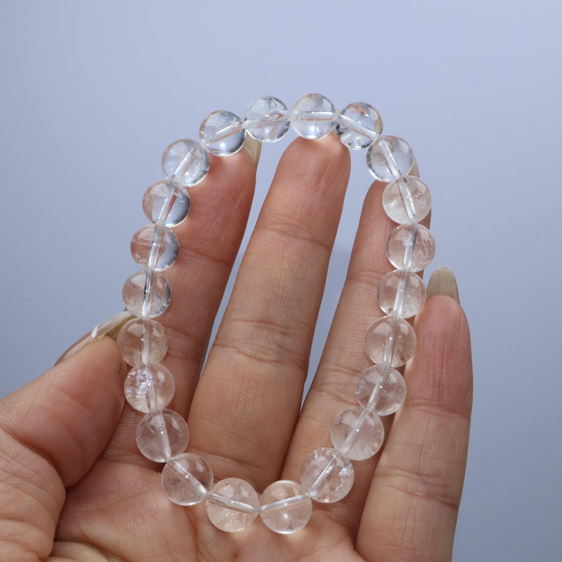 Handheld view of Clear Quartz bracelet showcasing round transparent beads with natural inclusions