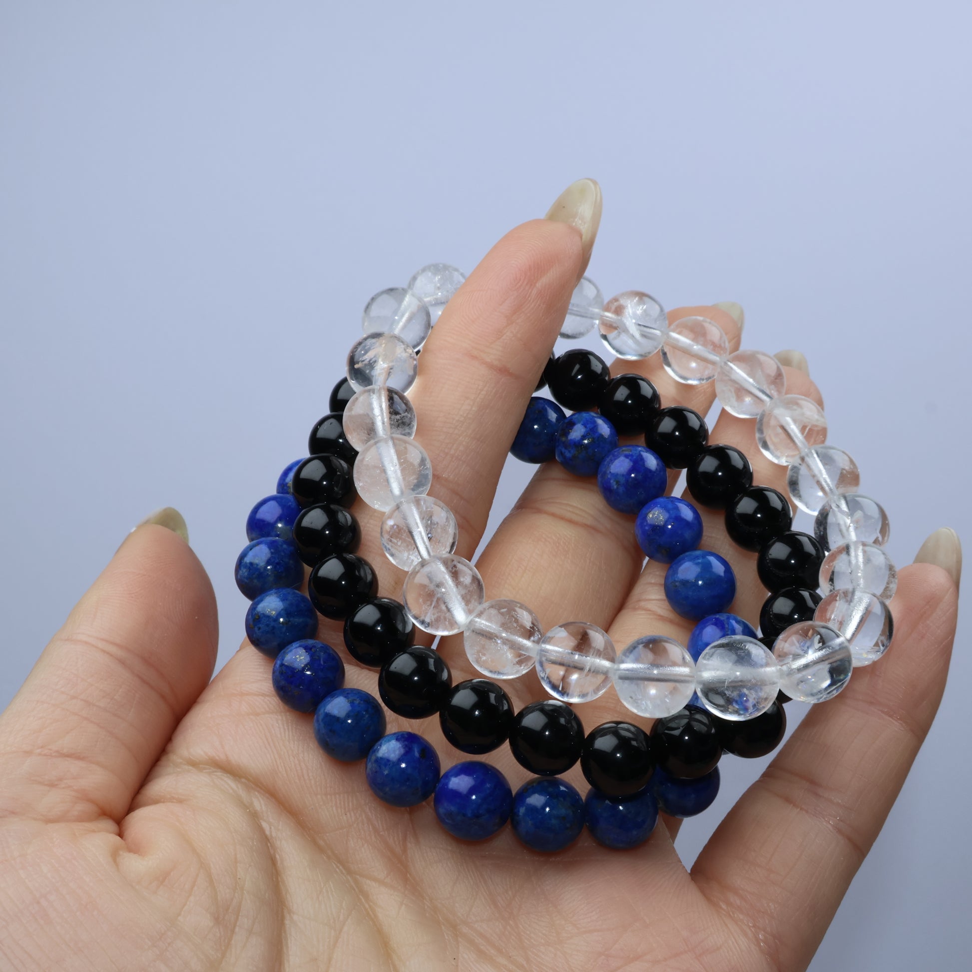 Handheld stack of three crystal bracelets – Lapis Lazuli, Clear Quartz, and Obsidian – showing color contrast and bead clarity