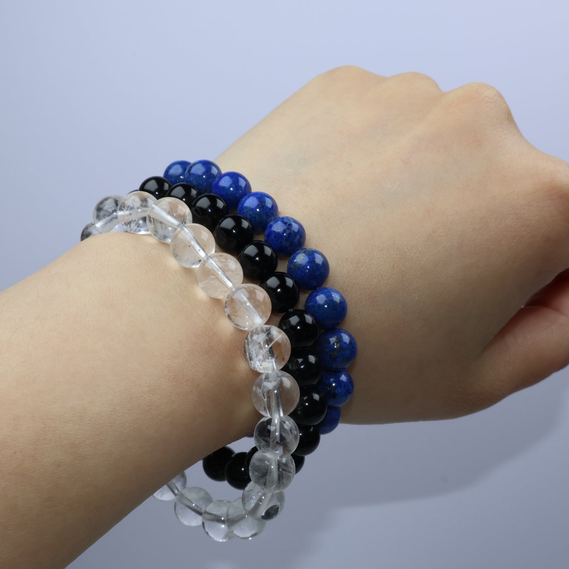 Side view of hand wearing three stacked bracelets with a minimalist background