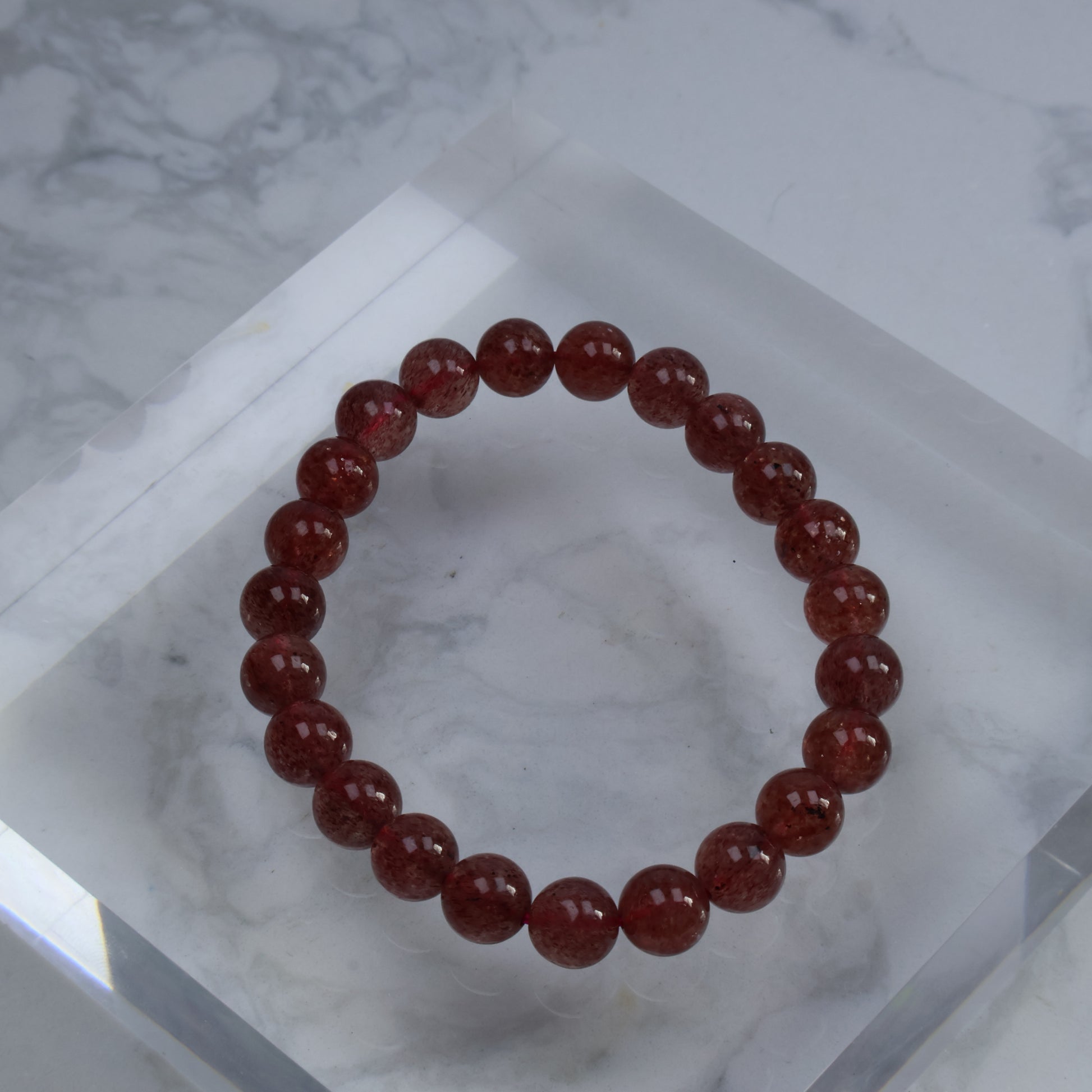 Top view of 8mm Strawberry Quartz bracelet on acrylic block with visible red inclusions