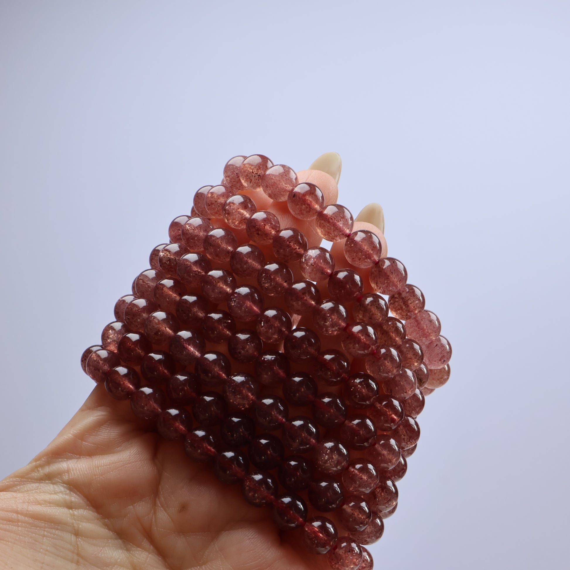 Multiple Strawberry Quartz bracelets stacked in hand, showing color variation