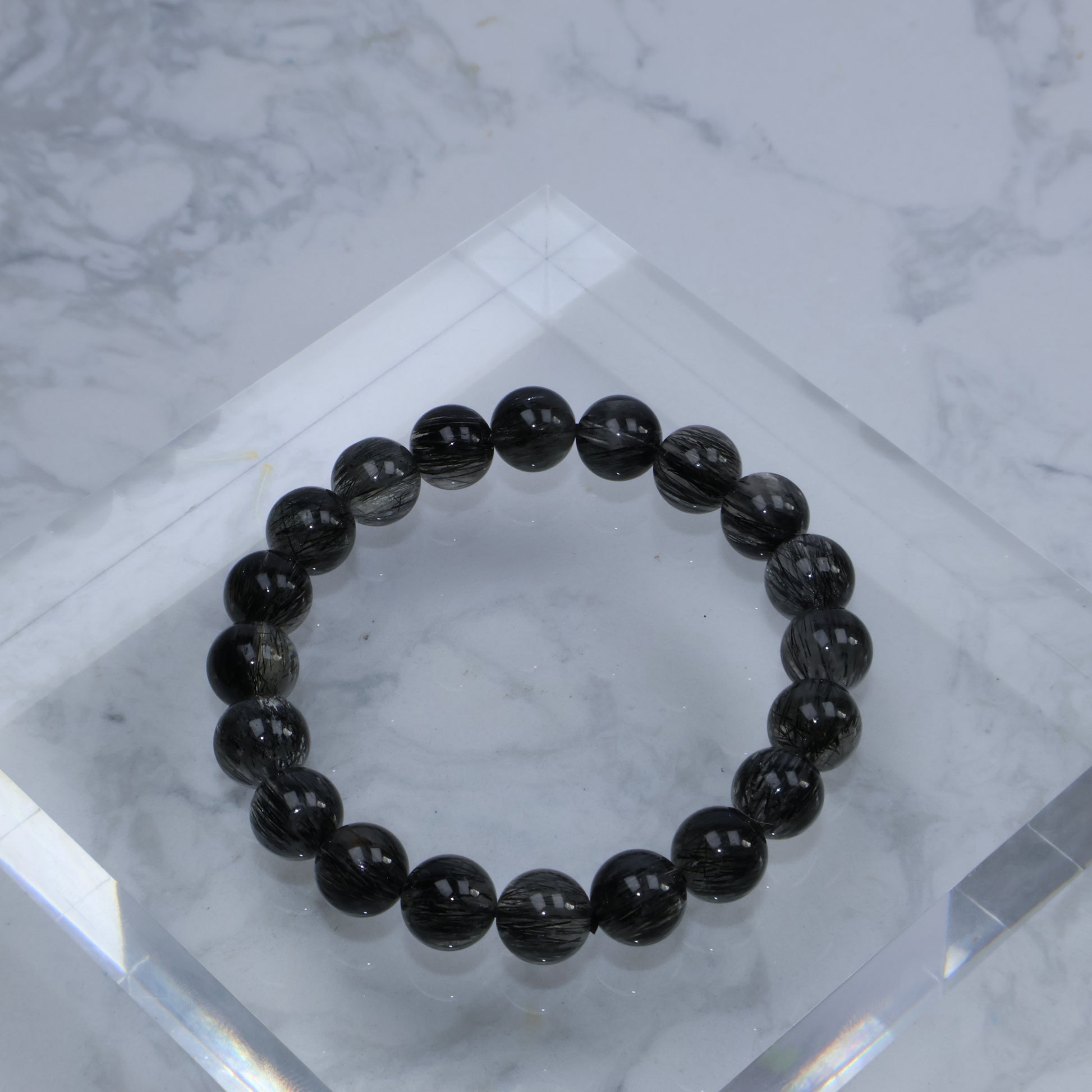 Top-down view of 9mm Black Rutilated Quartz bracelet on acrylic block
