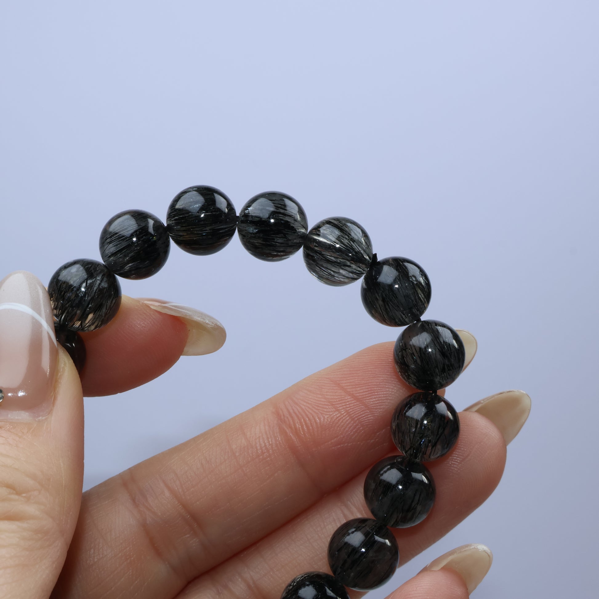 Handheld view of Black Rutilated Quartz beads with visible rutile strands and slight cloudiness