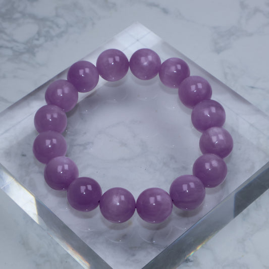 Top-down photo of pastel lavender Lepidolite bracelet on a clear acrylic cube with marble background