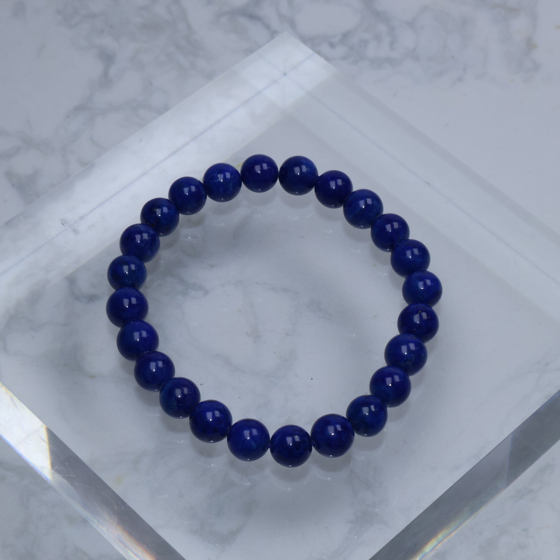 Top-down photo of a round Lapis Lazuli bracelet with deep royal blue color on a clear acrylic block