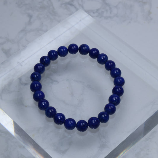Top-down photo of a round Lapis Lazuli bracelet with deep royal blue color on a clear acrylic block