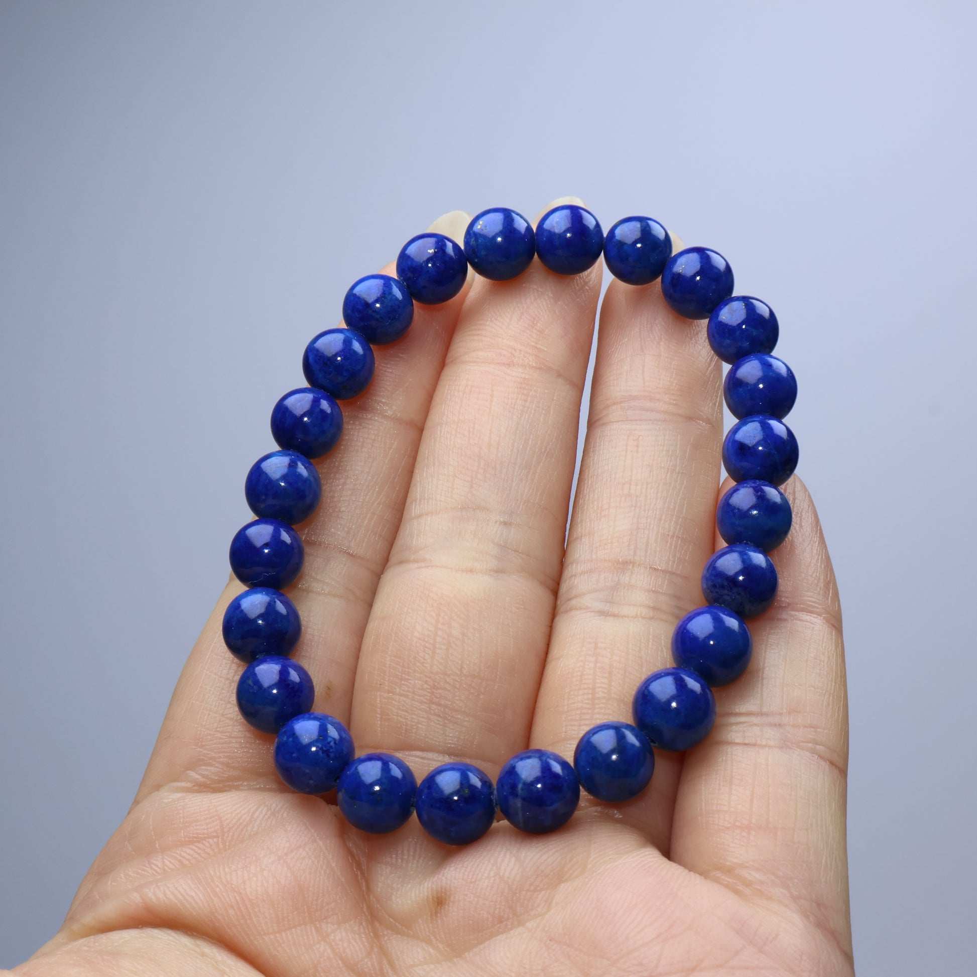 Handheld view of a dark blue Lapis Lazuli bracelet with smooth, polished beads
