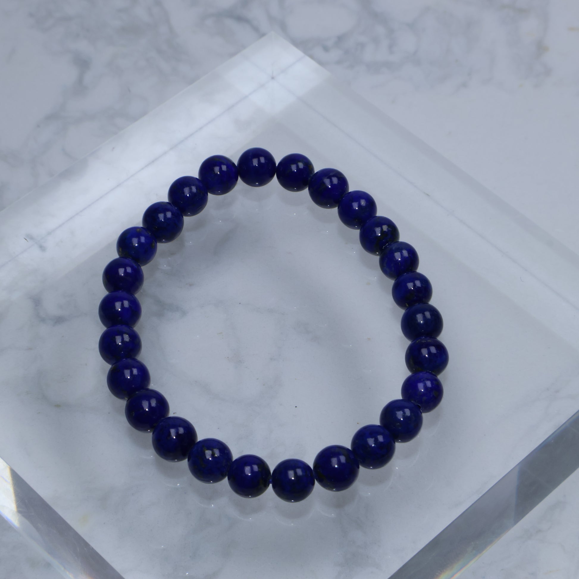 Top-down photo of Lapis Lazuli bracelet with deep royal blue color on acrylic block