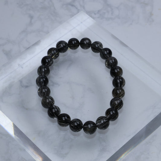 Top-down view of glossy Black Rutilated Quartz bracelet arranged on a clear acrylic block