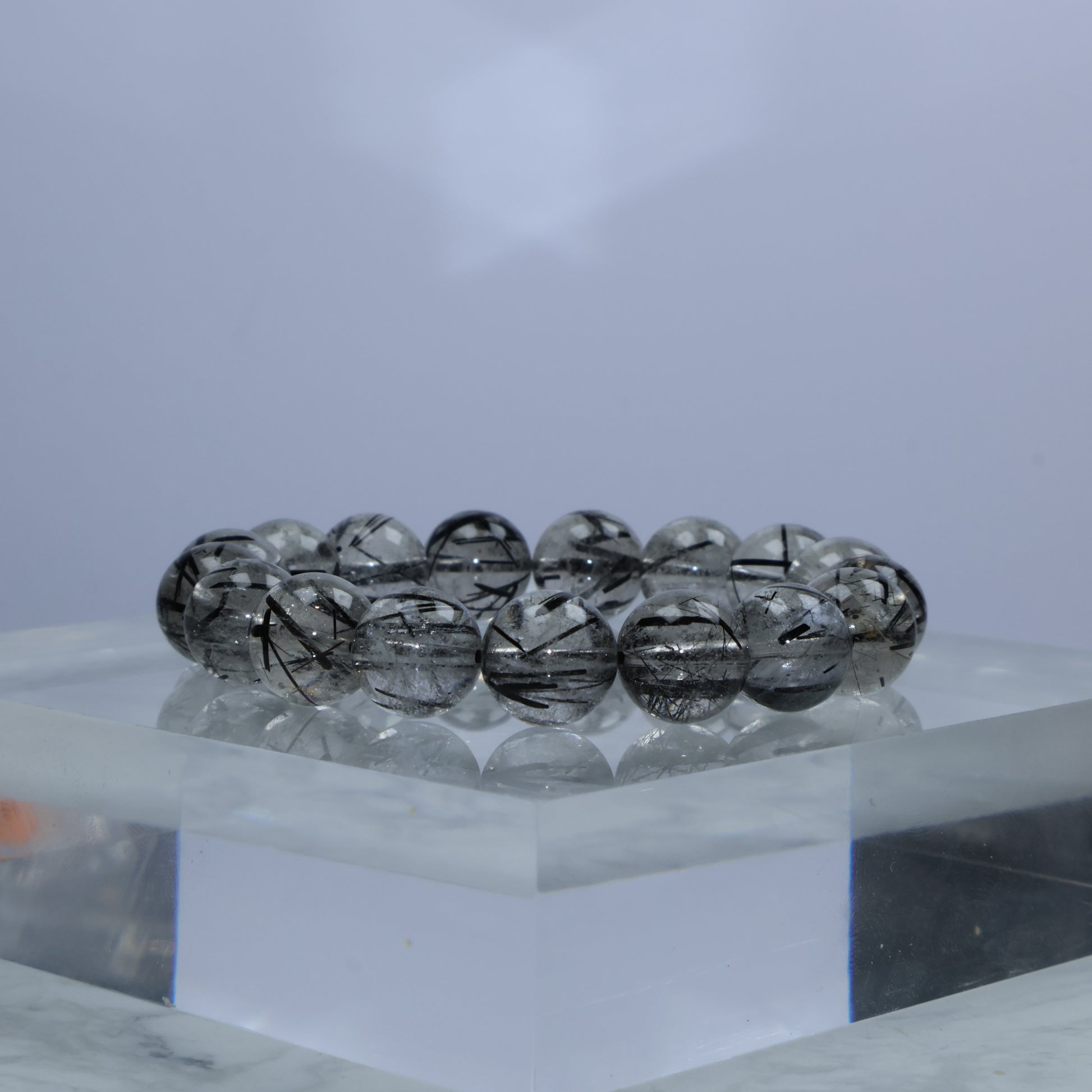 Side angle of 11mm Black Rutilated Quartz bracelet on acrylic block with clear rutile threads inside beads