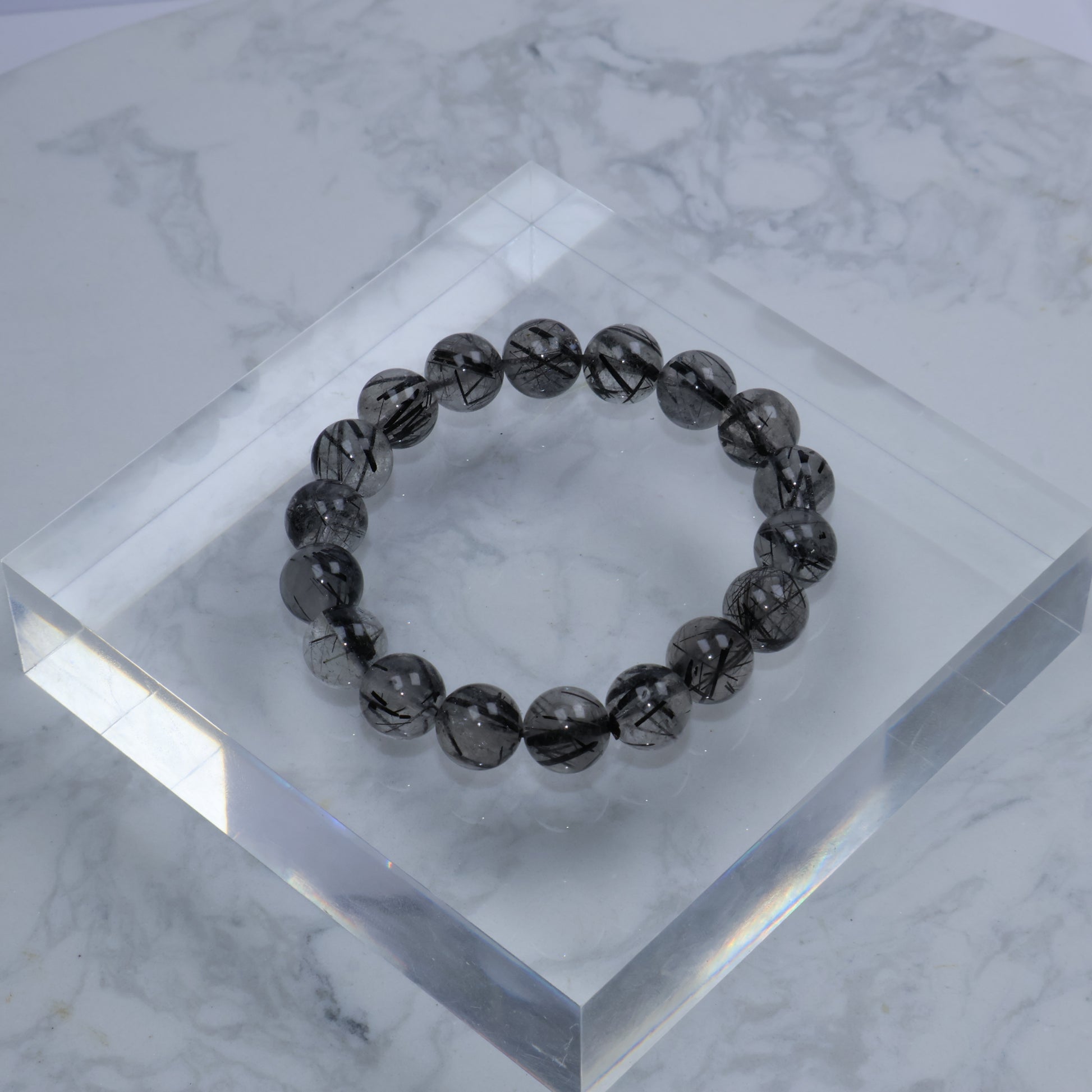 Top-down view of 10mm Black Rutilated Quartz bracelet on clear acrylic block