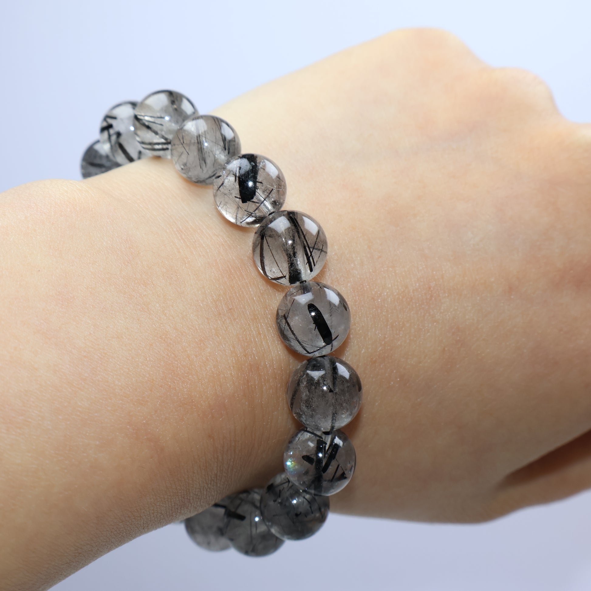 Wrist shot of 10mm Black Rutilated Quartz bracelet showing bold rutile threads and cotton inclusions inside semi-translucent beads