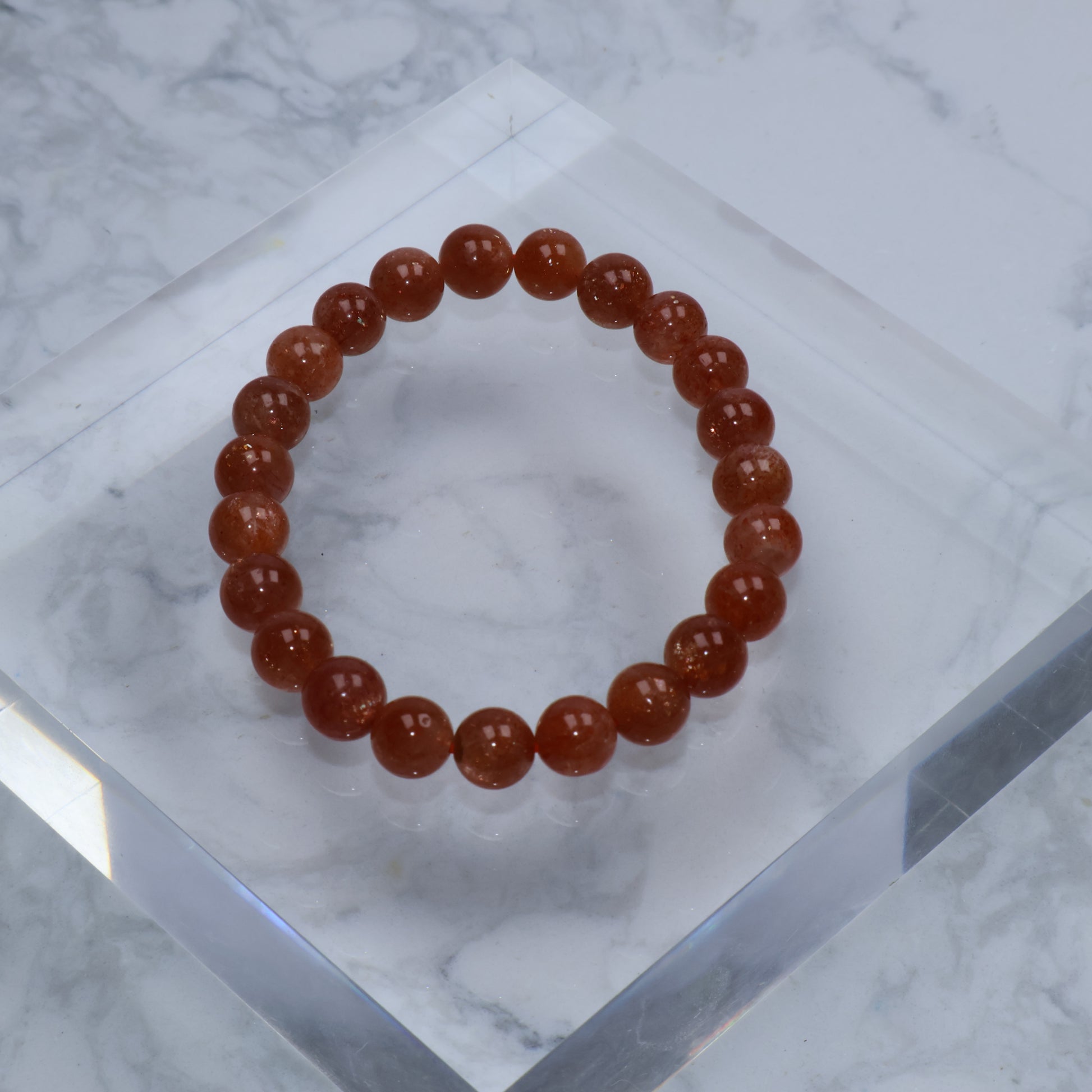 Top-down image of deep orange 8mm Sunstone bracelet on acrylic block