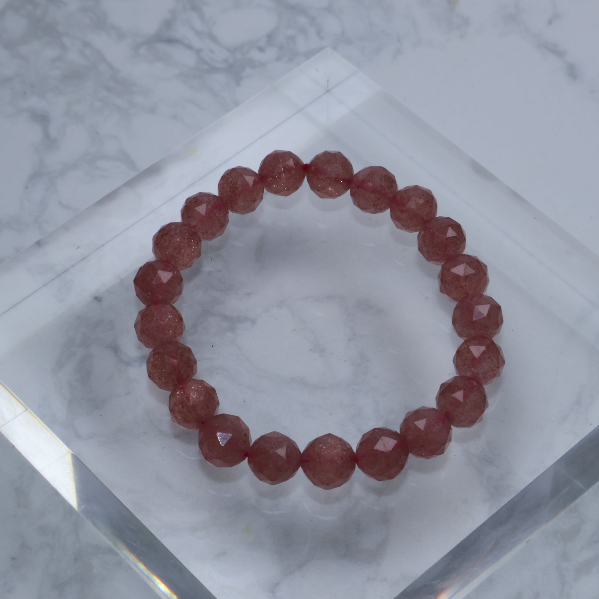 Top-down photo of faceted Strawberry Quartz bracelet on clear acrylic block
