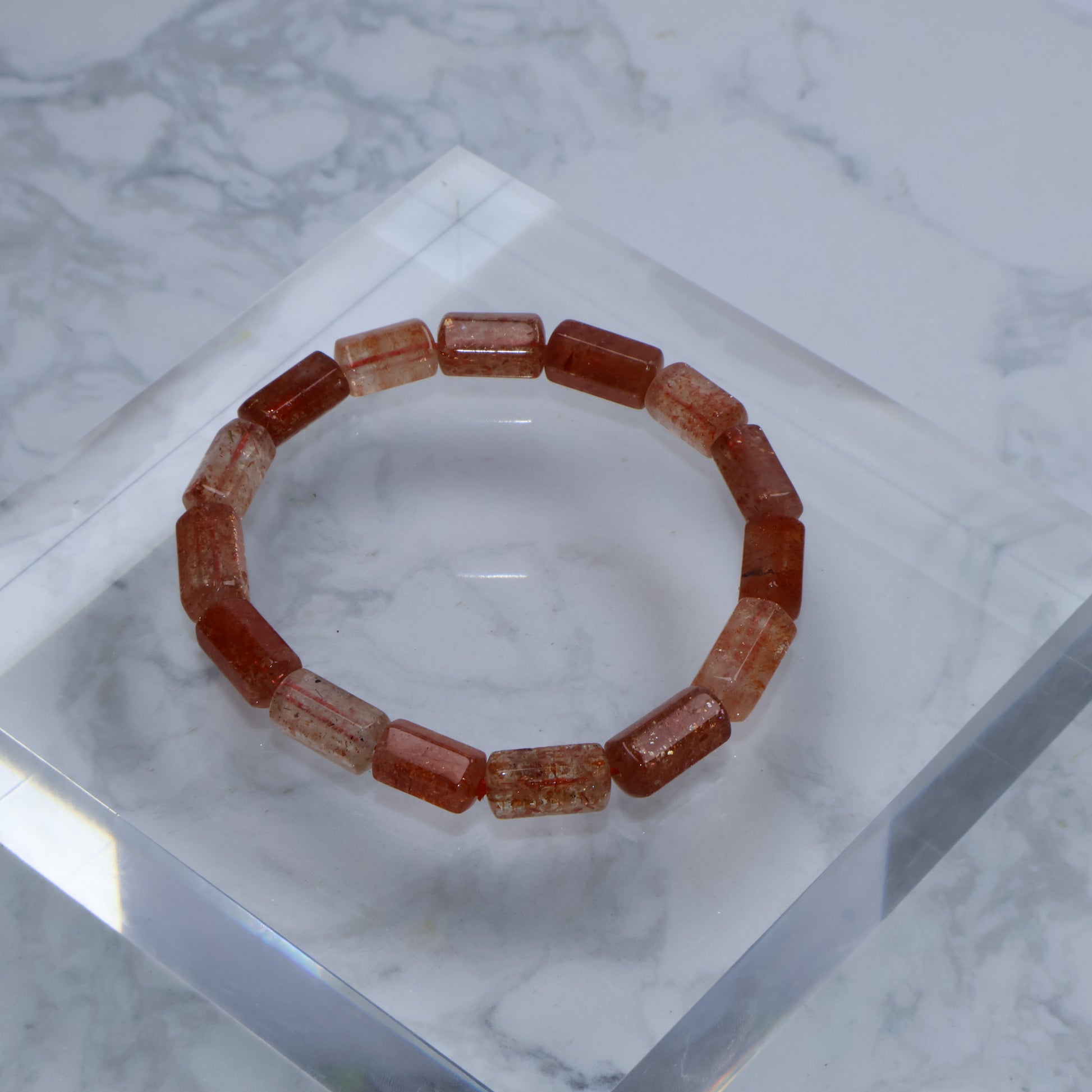 Top view of Sunstone barrel bead bracelet placed on clear acrylic block, highlighting warm orange tones